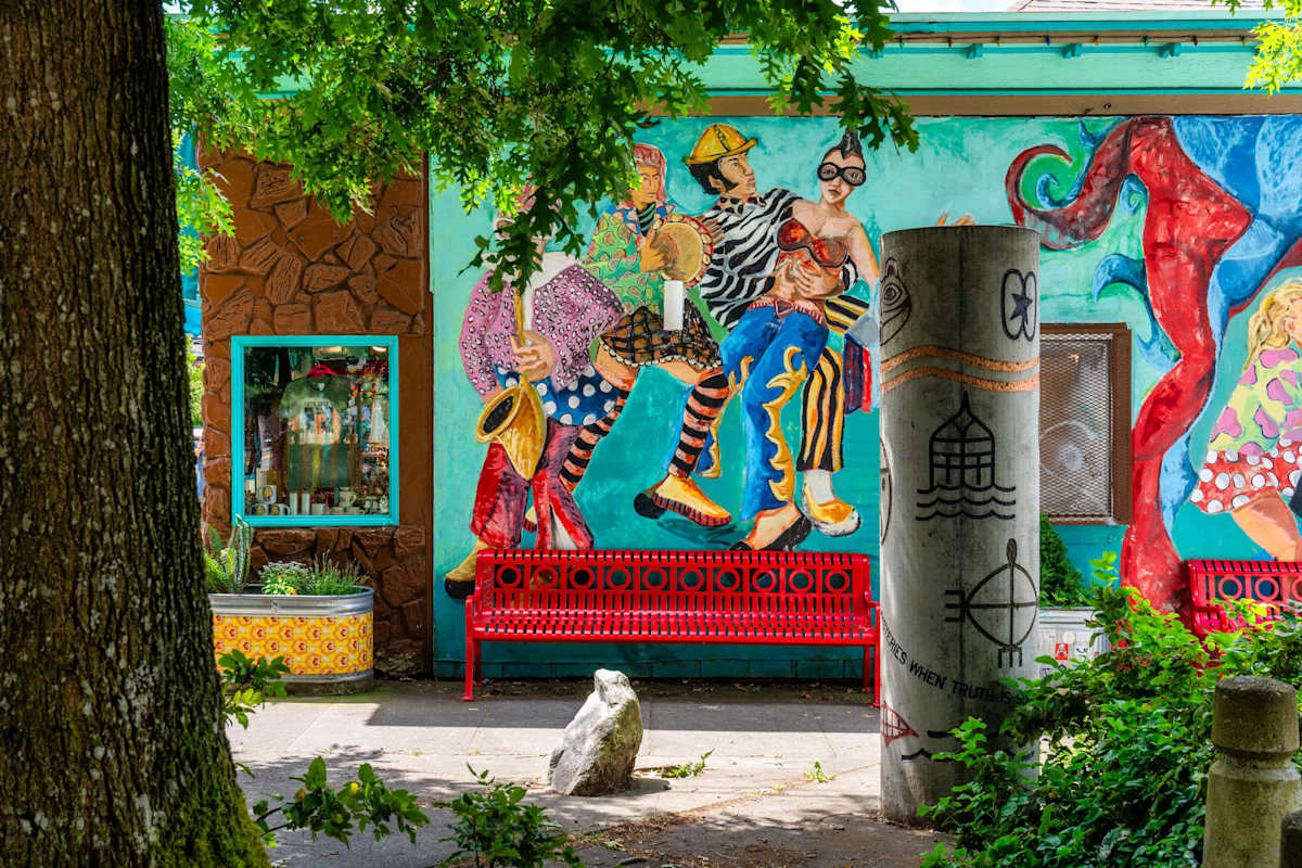 A colorful mural on the side of a building with a red bench and a tree in front of it.