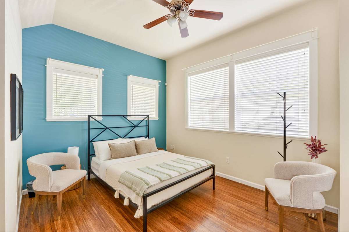 A neatly arranged bedroom with a double bed, two chairs, and a ceiling fan.