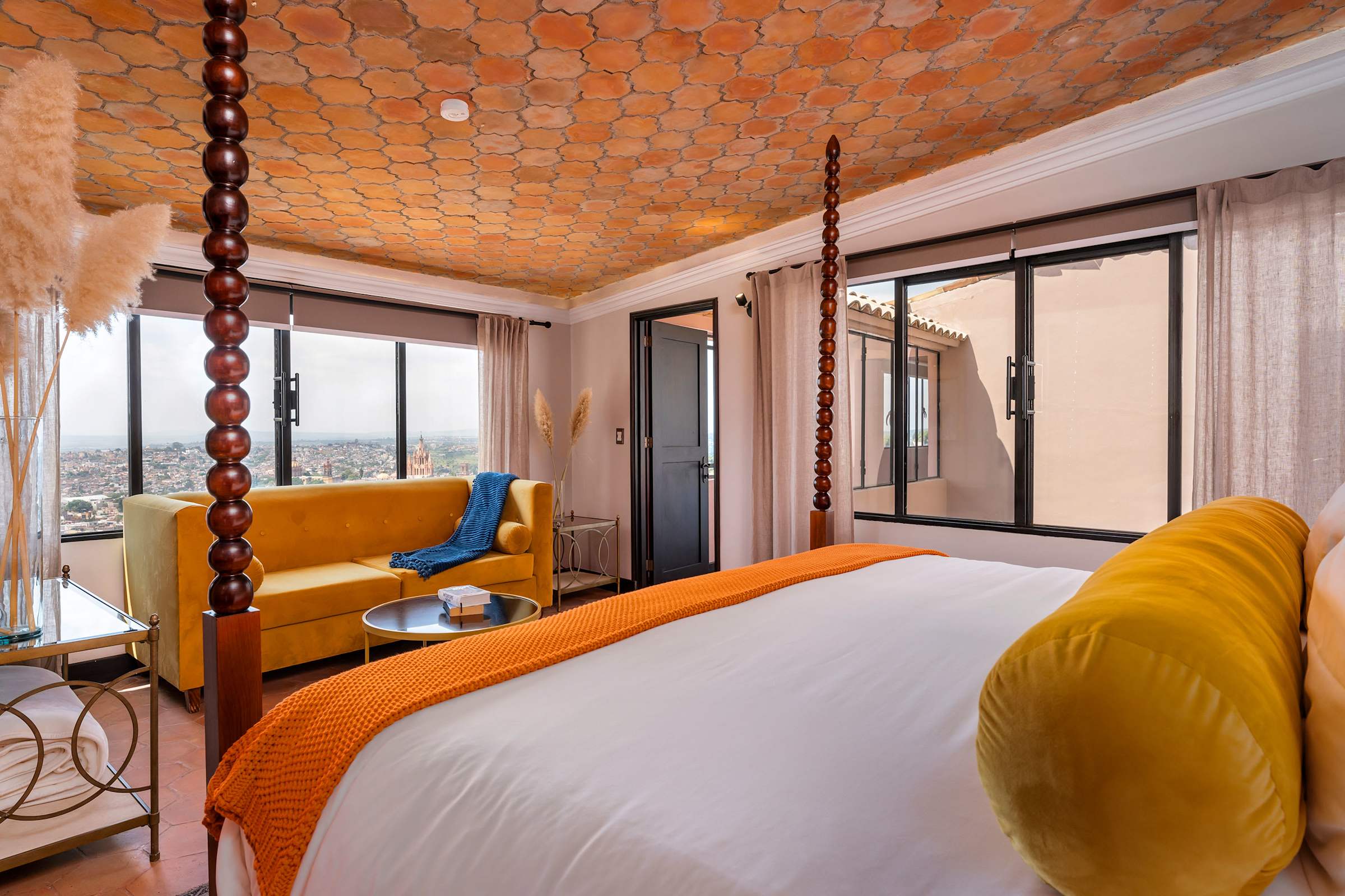 King bedroom with yellow accent sofa and windows overlooking the city