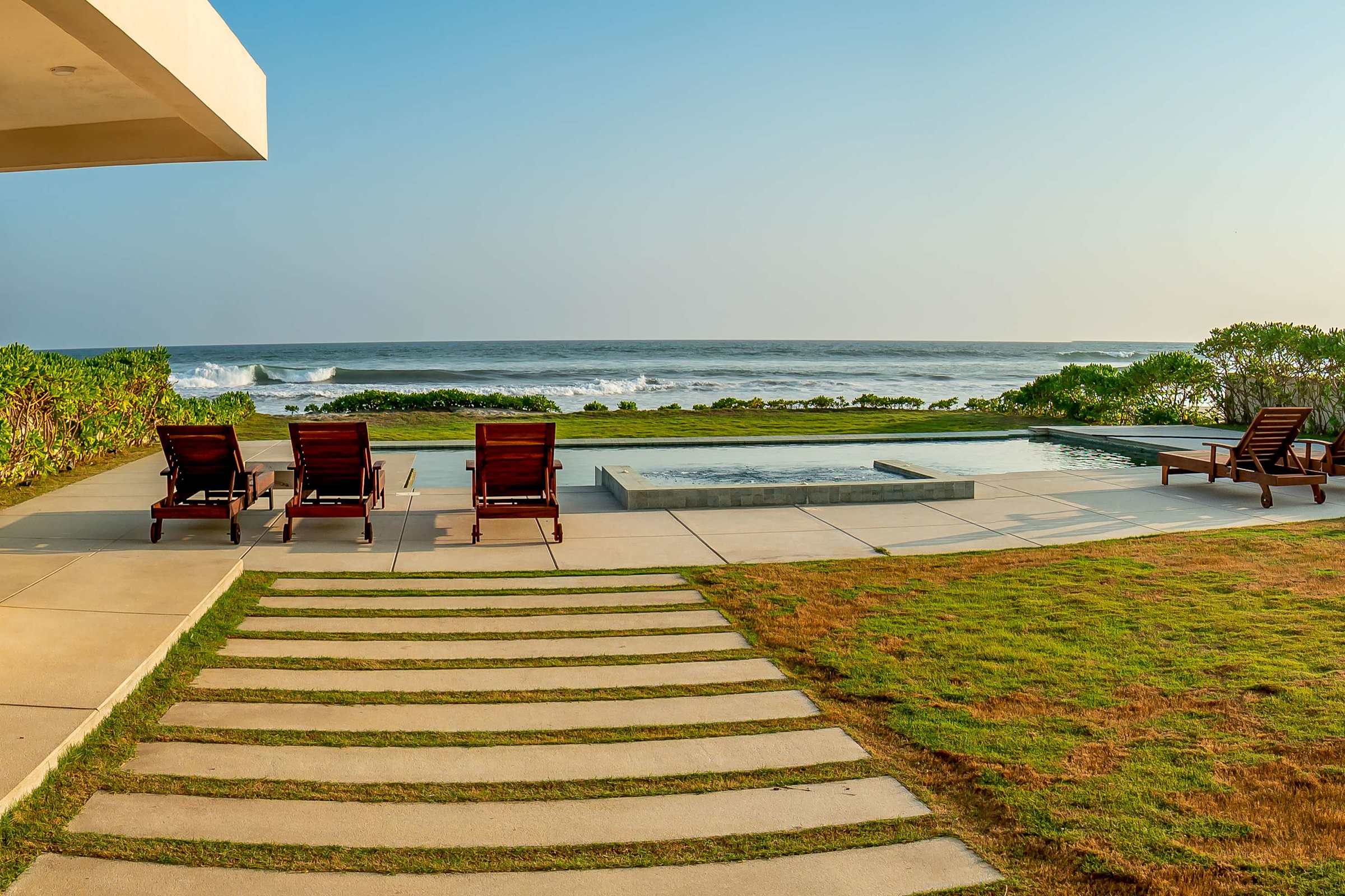 Wide daytime view of the villa's pool, sun deck, lush lawns, and private beach access — endless outdoor space to enjoy