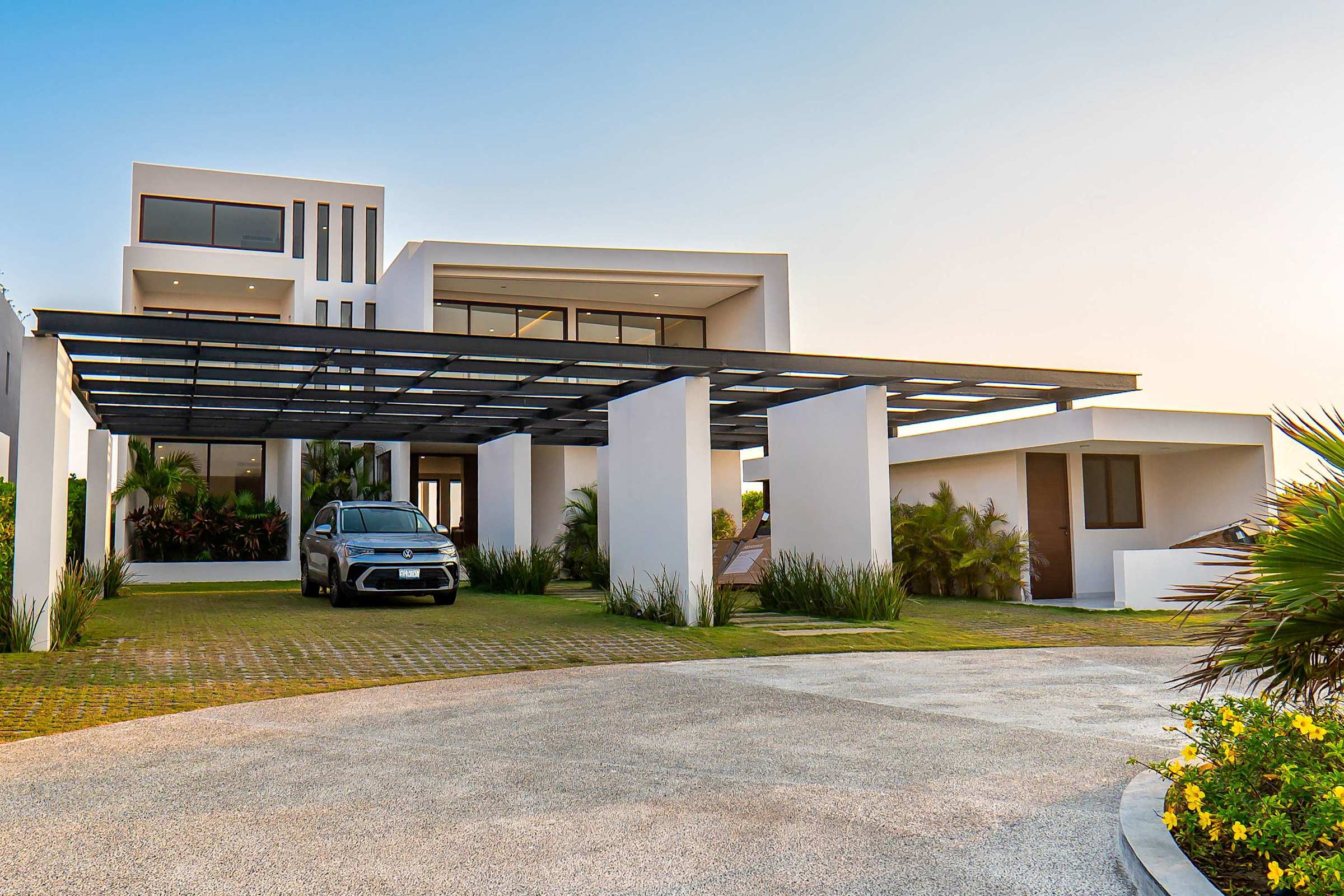 Villa entrance and driveway with lush tropical landscaping and the estate's striking modern architecture. Includes parking for 6 cars.