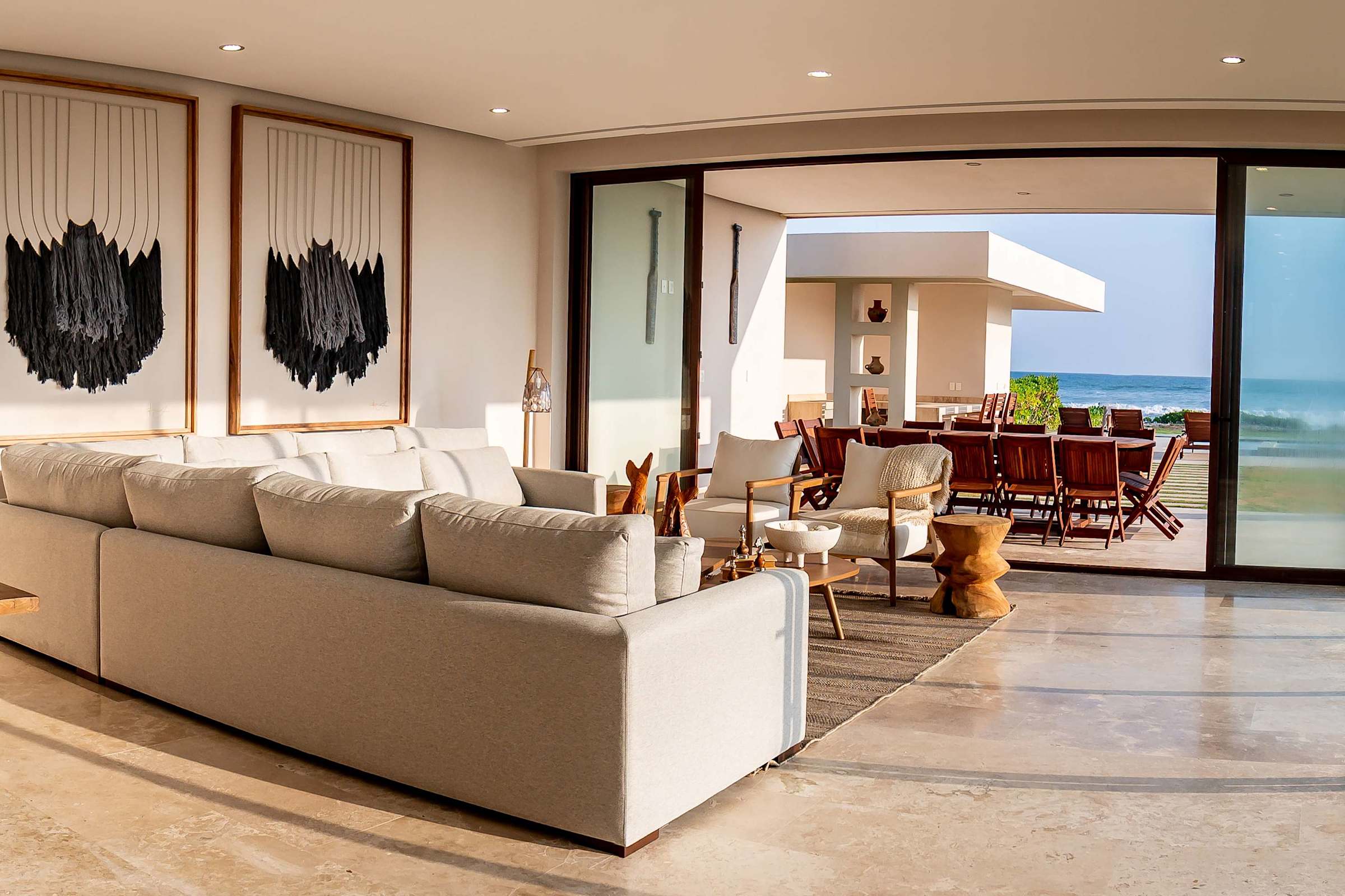 Open-plan living area with floor-to-ceiling glass doors, modern sofas, and direct ocean views — bring the outdoors in