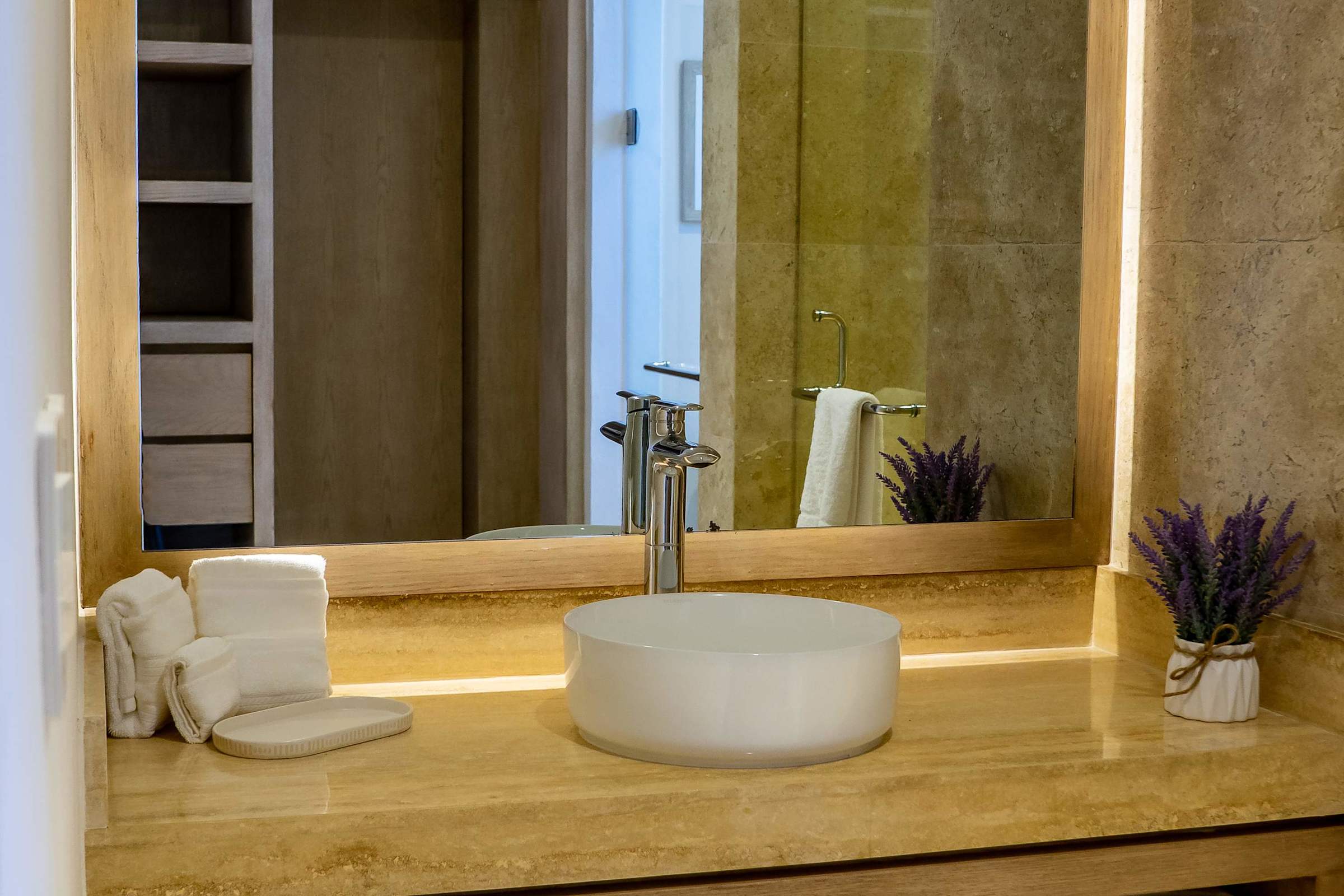 Luxurious marble-tiled bathroom with a wooden wardrobe and shower, warm gold tones, and lush plant accents