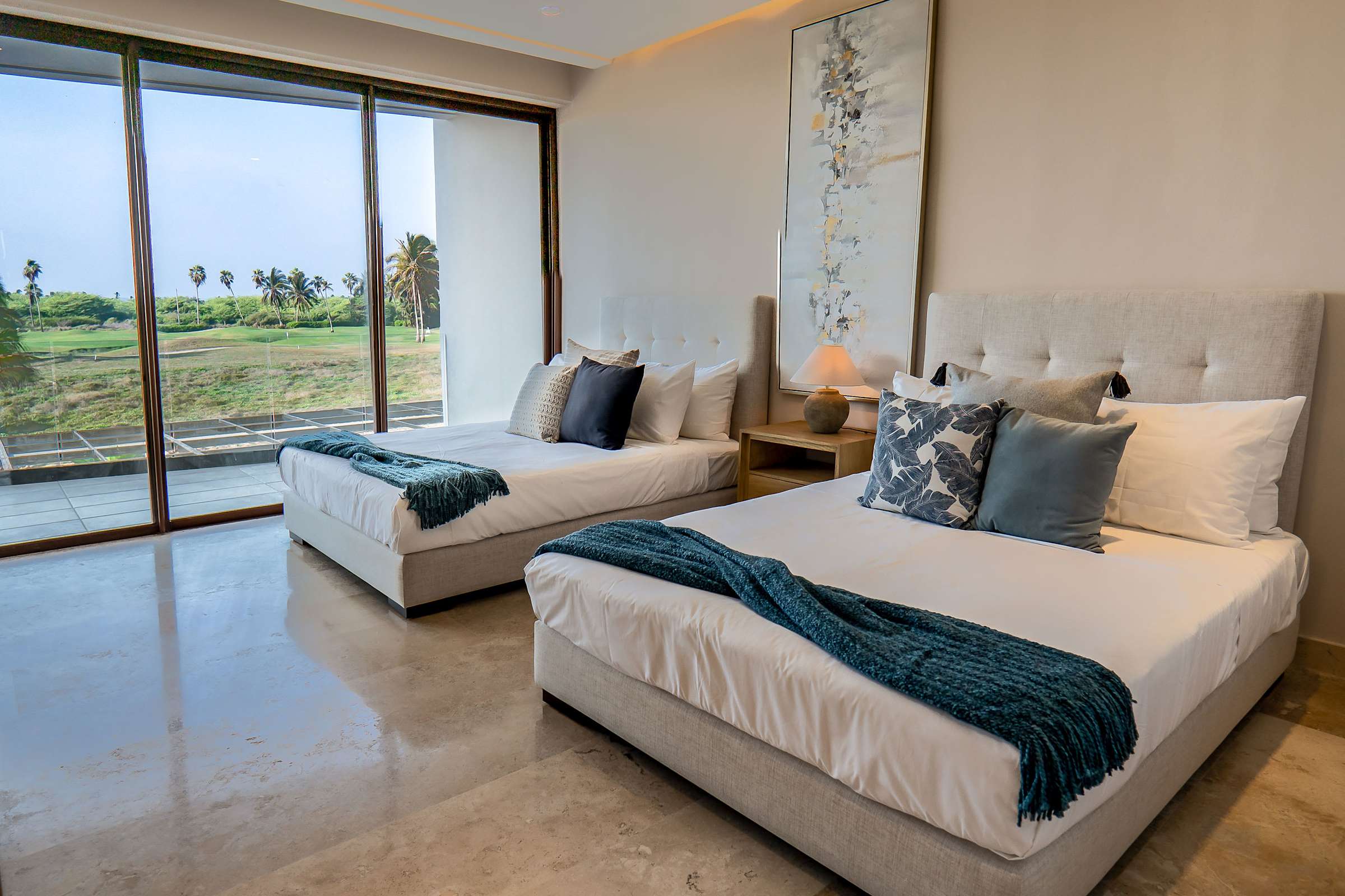 Bedroom 7 with two queen beds, tropical artwork, teal linens, and sliding glass doors to a private terrace that overlooks the golf course