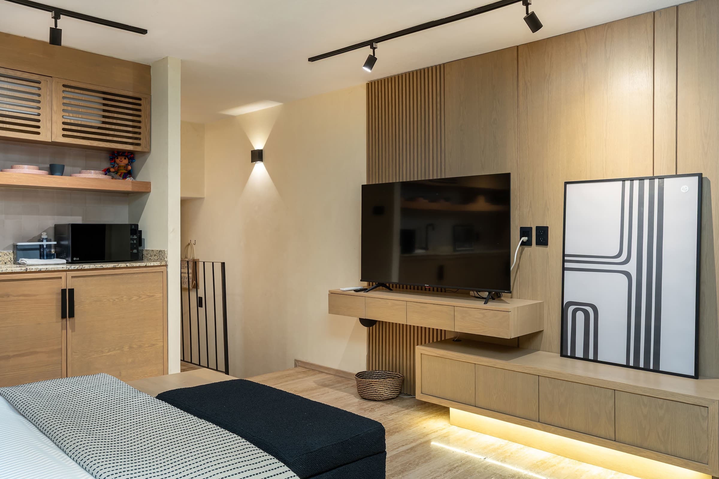 Bedroom overview showing the queen and twin bed arrangement & TV alongside wood built-in storage and the kitchenette, with the hallway entry.