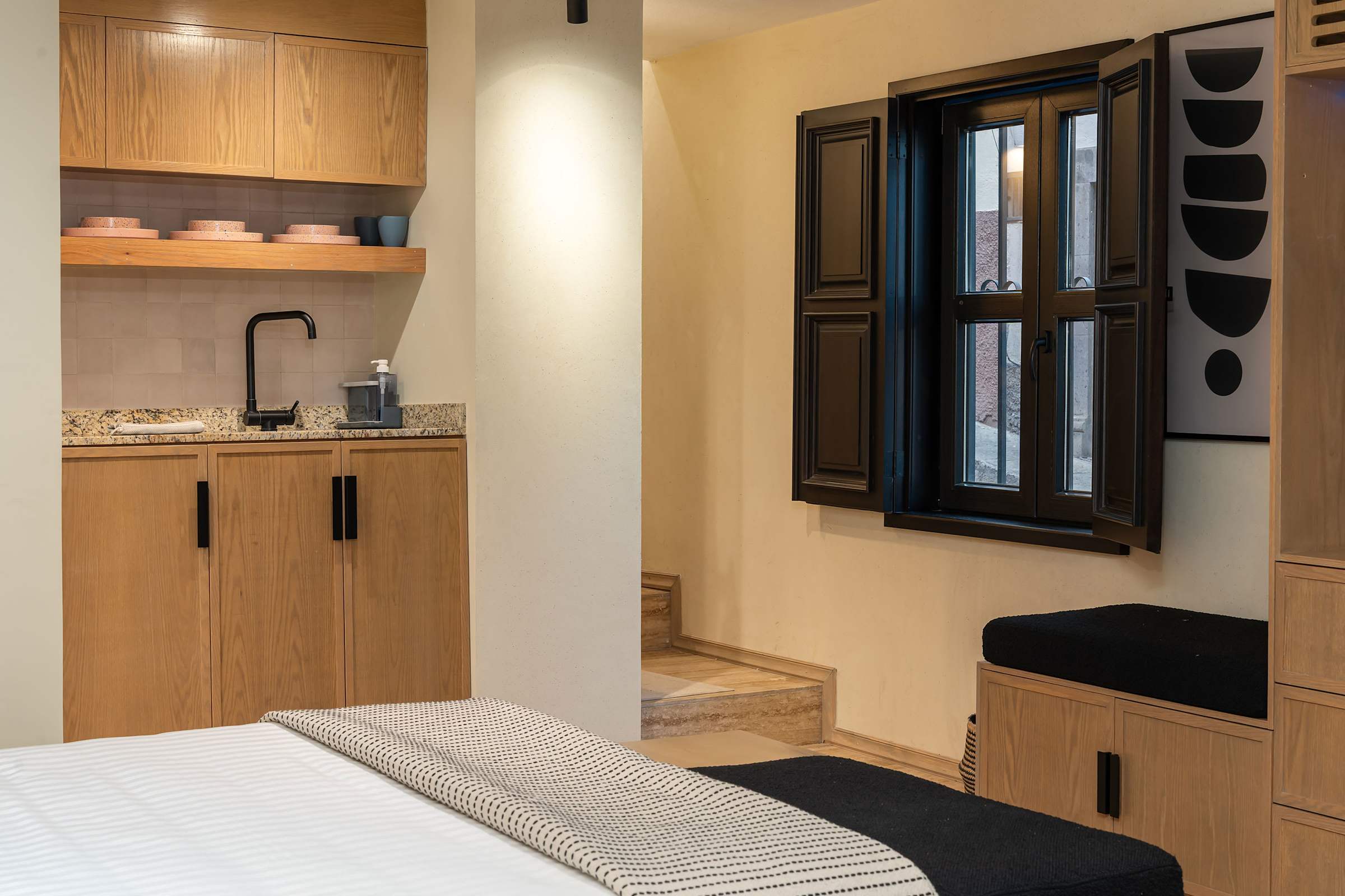 Bedroom kitchenette with wood cabinetry, a faucet sink, microwave, and a traditional shuttered window with street views.