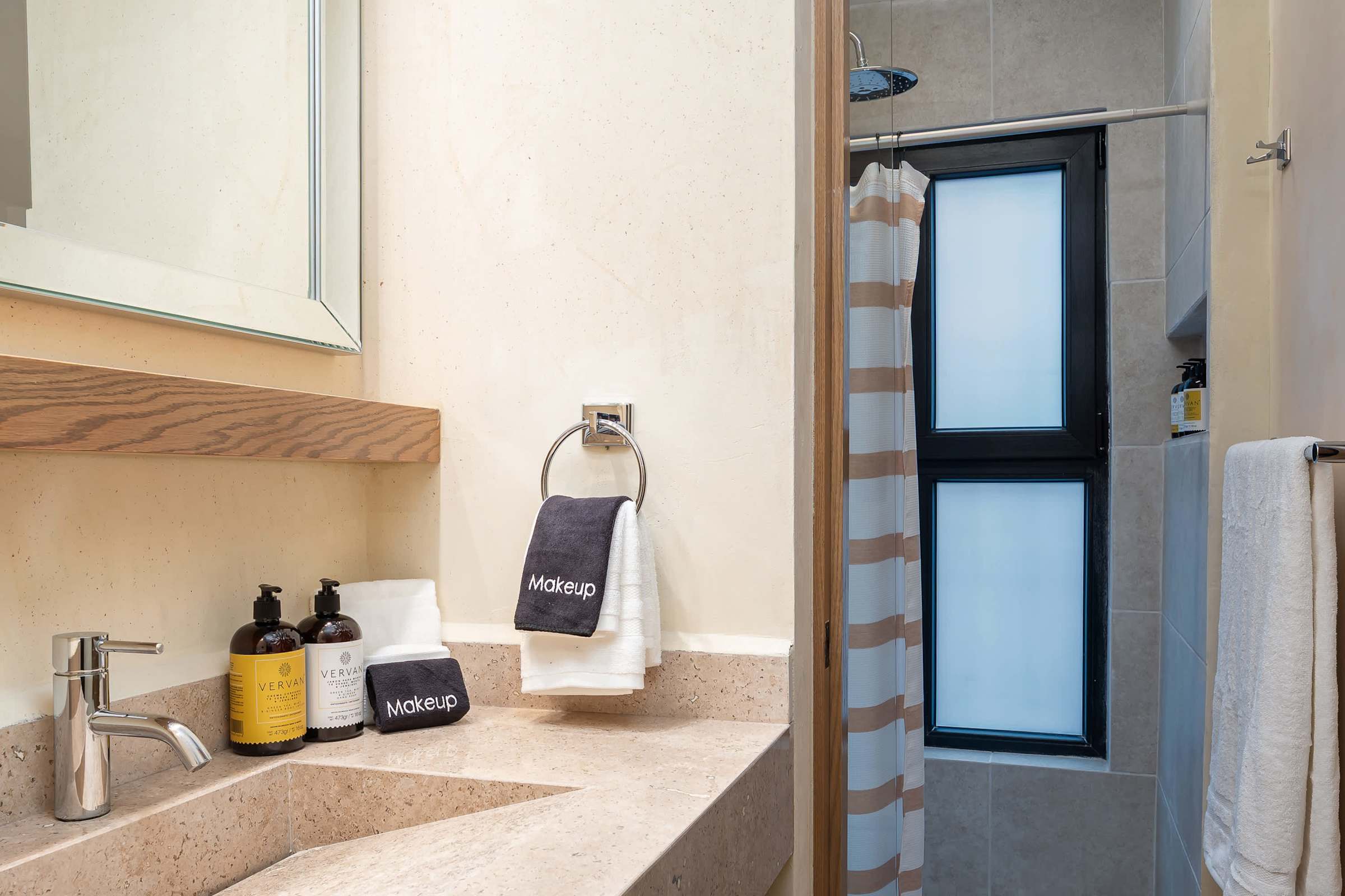 Ensuite bathroom with a marble stone vanity, soap and shampoo amenities, towels, a mirror above the sink, with a toilet and shower.