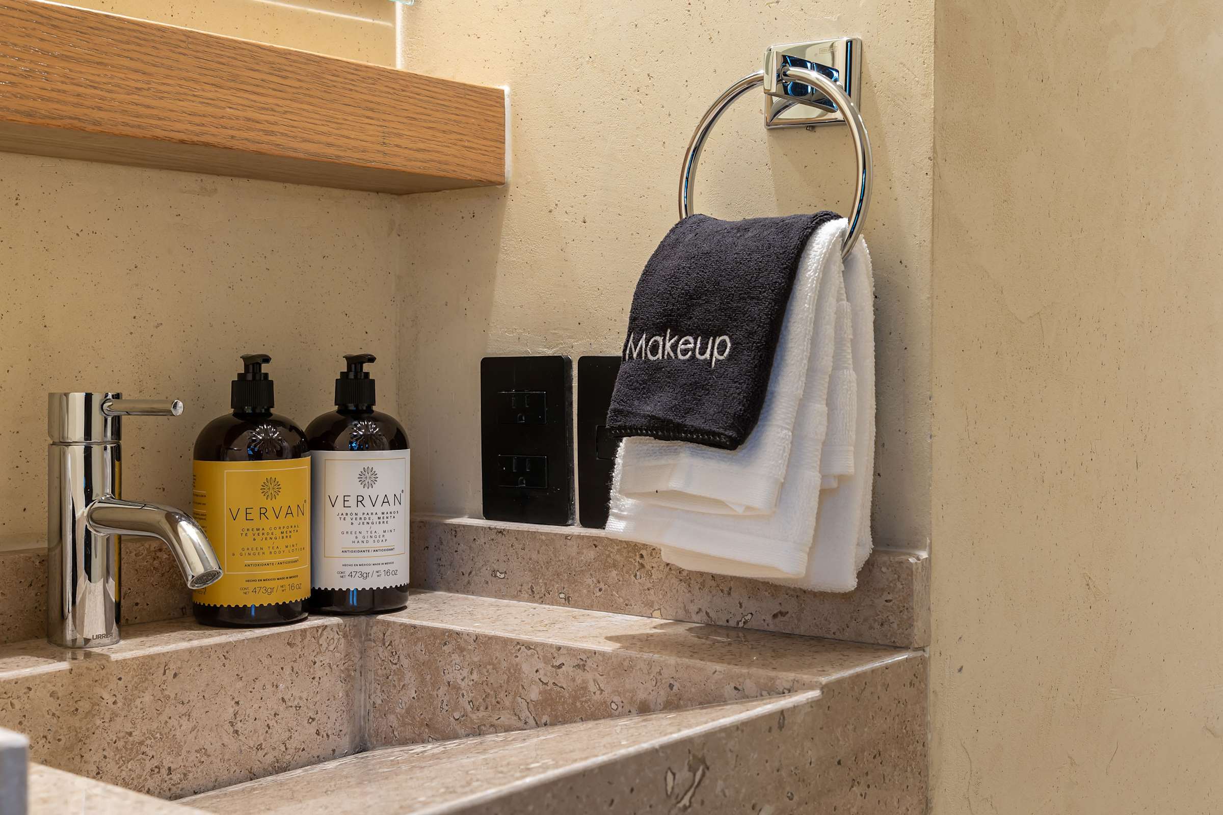 Close-up of the ensuite bathroom vanity with a granite sink, premium soap dispensers, chrome fixtures, and towels.