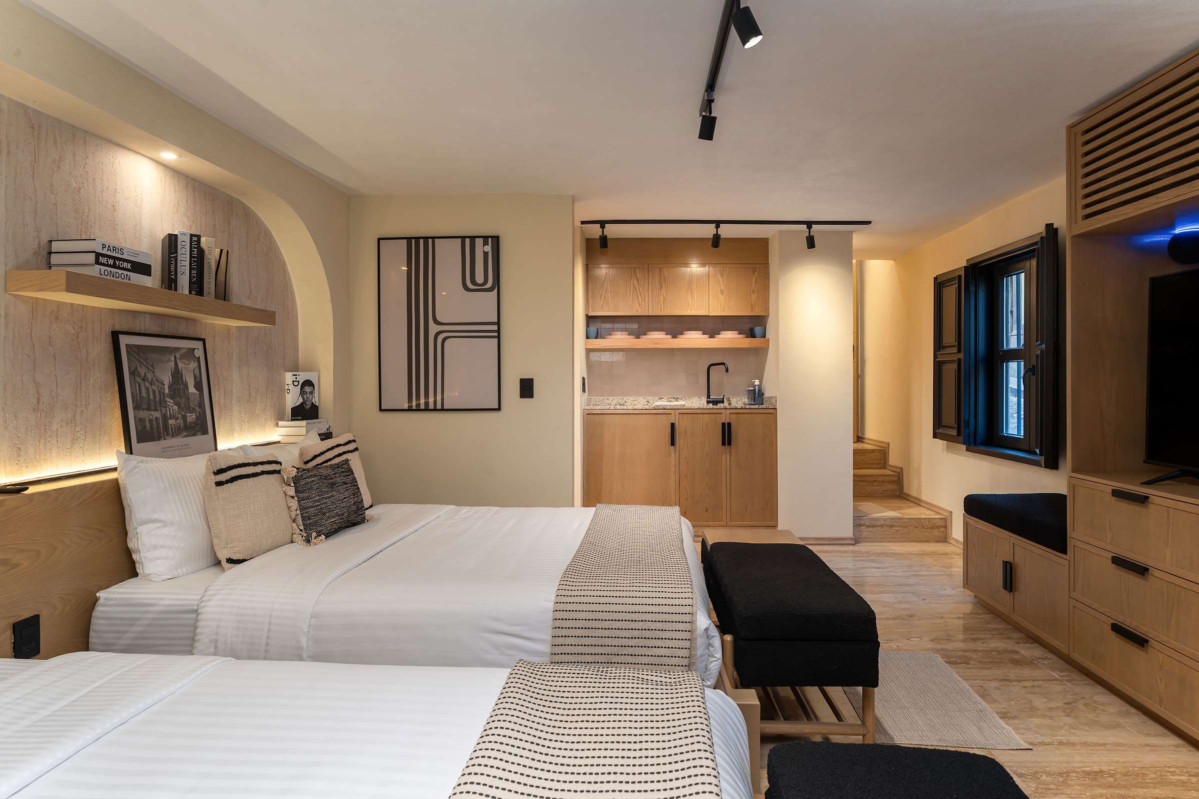 Bedroom overview with both queen beds, large windows, wall shelf with framed photos, and a TV with wood built-in dresser and storage.