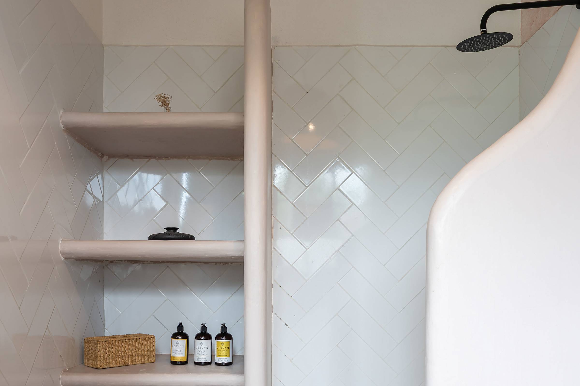 Walk-in shower with herringbone tile, rain showerhead, and built-in shelving