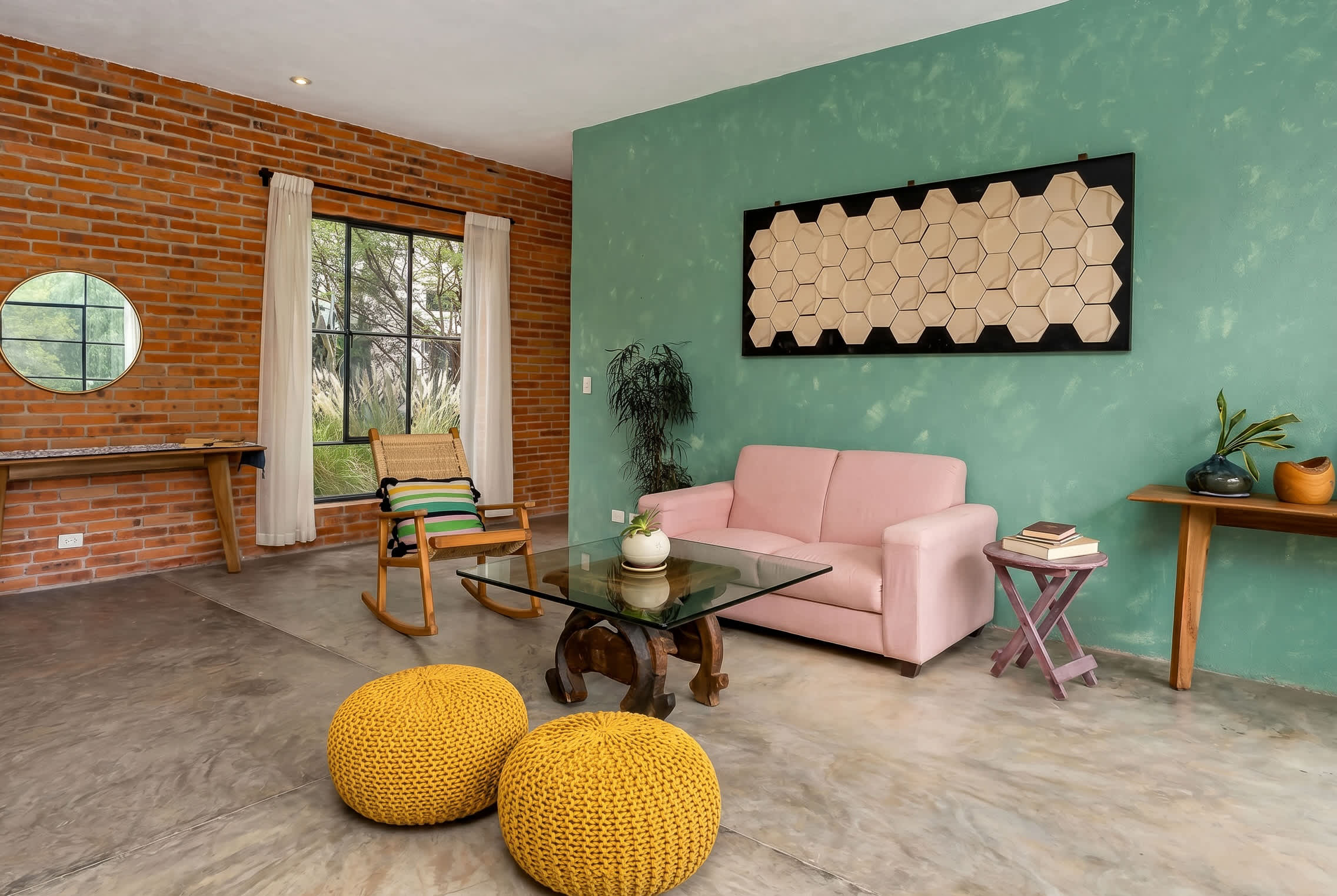 Living room with pink sofa, knit poufs, glass coffee table, and rocking chair