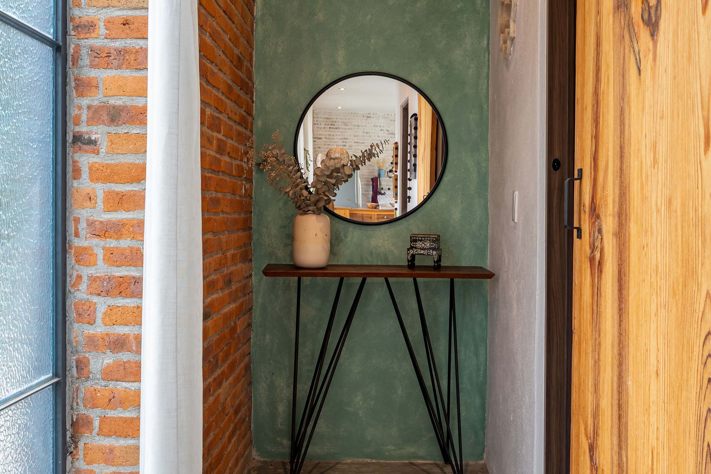 Hallway with round mirror, console table, and exposed brick wall