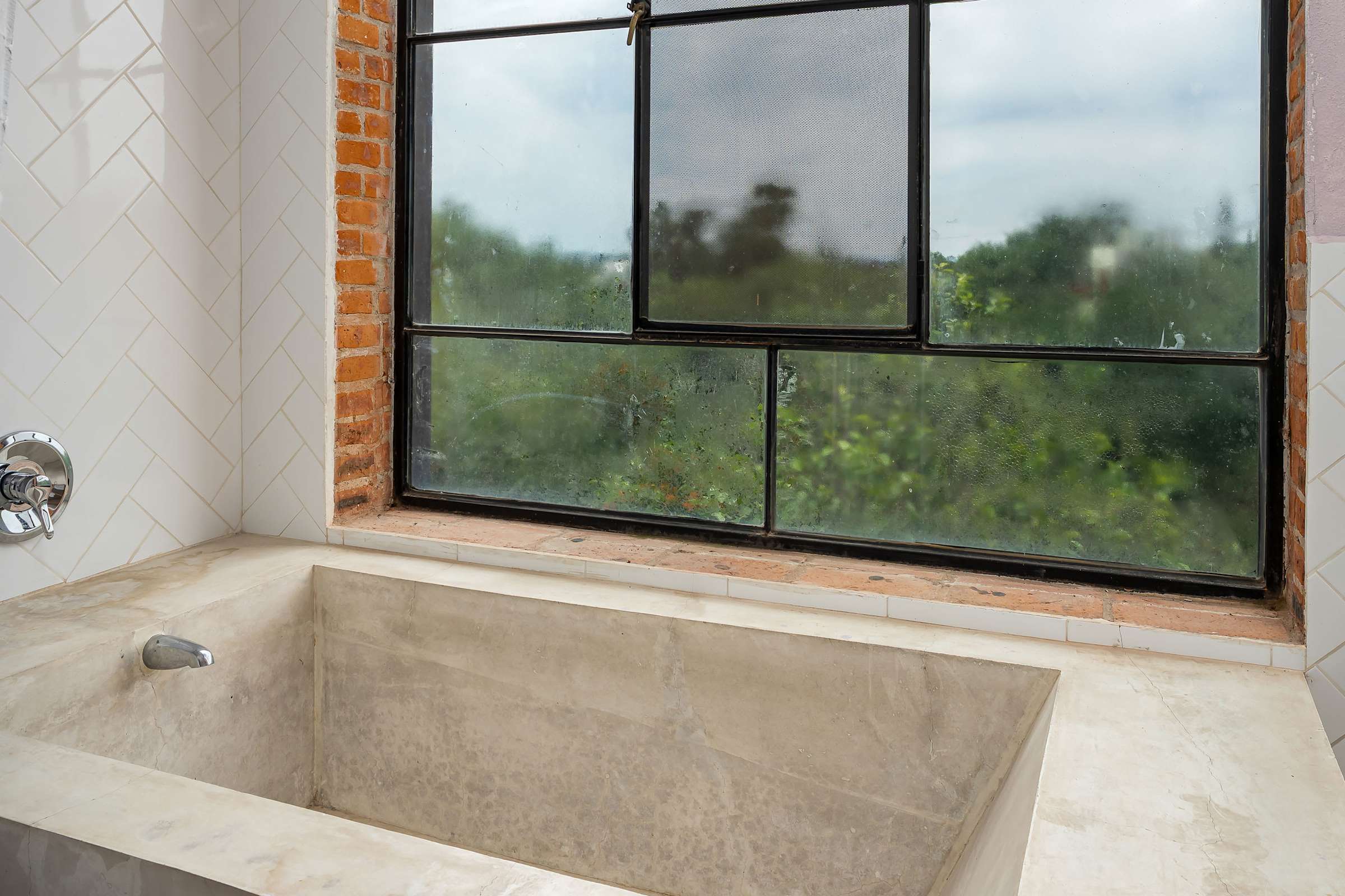 Deep soaking tub with garden views through large black-frame window