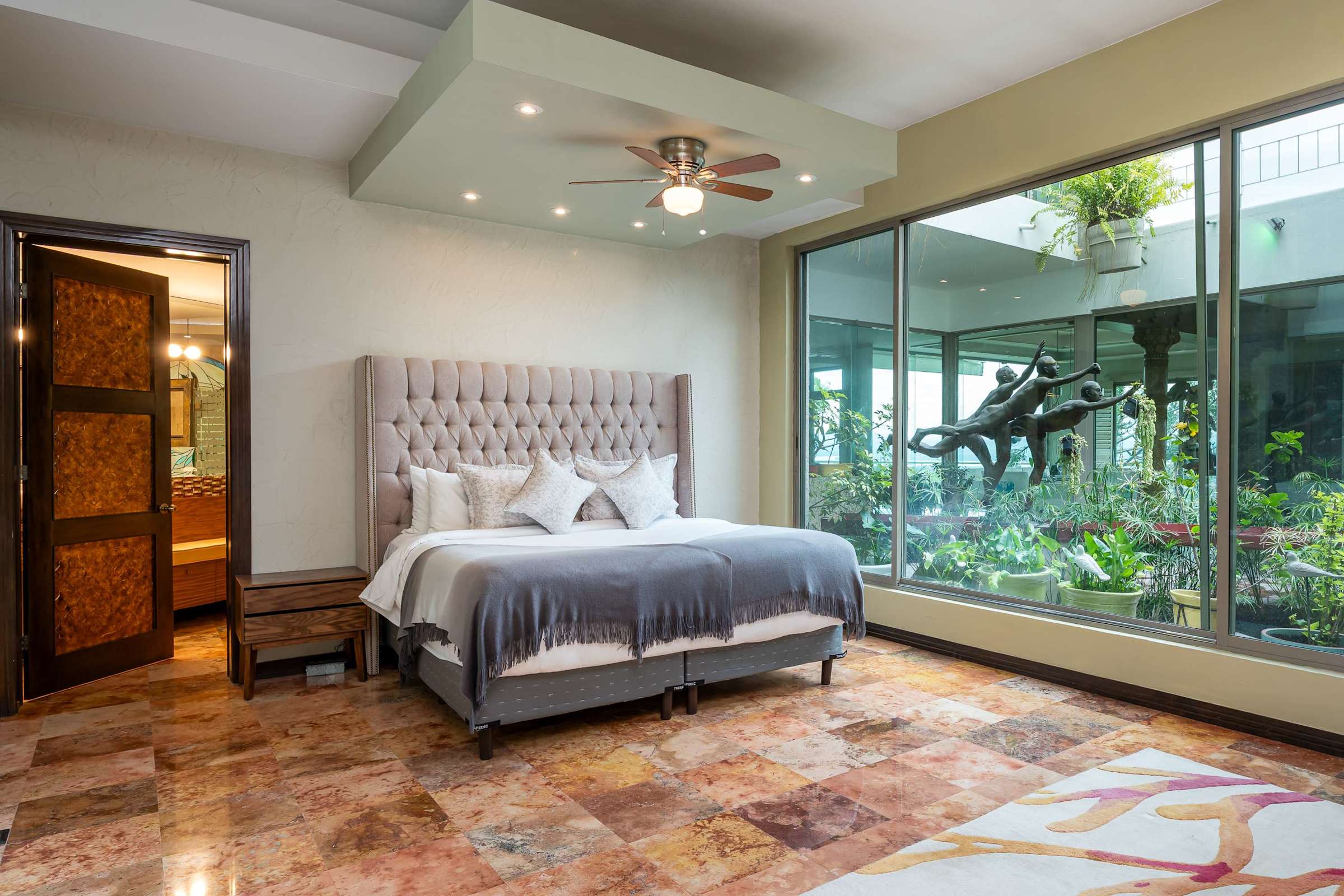 Primary bedroom with king bed, ensuite bathroom and glass walls with garden views