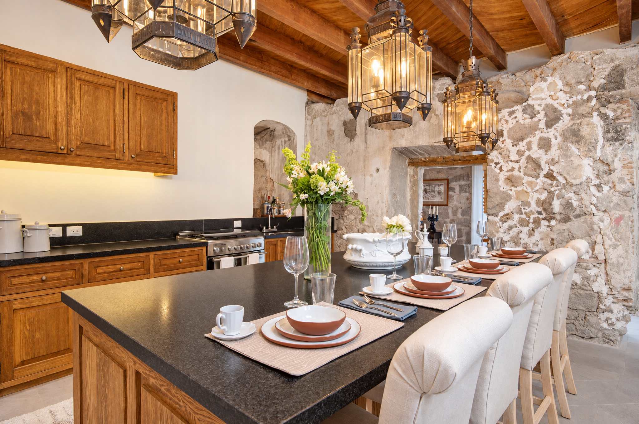 Cocina y comedor abiertos con vigas de madera, muros de piedra e isla con cubierta negra