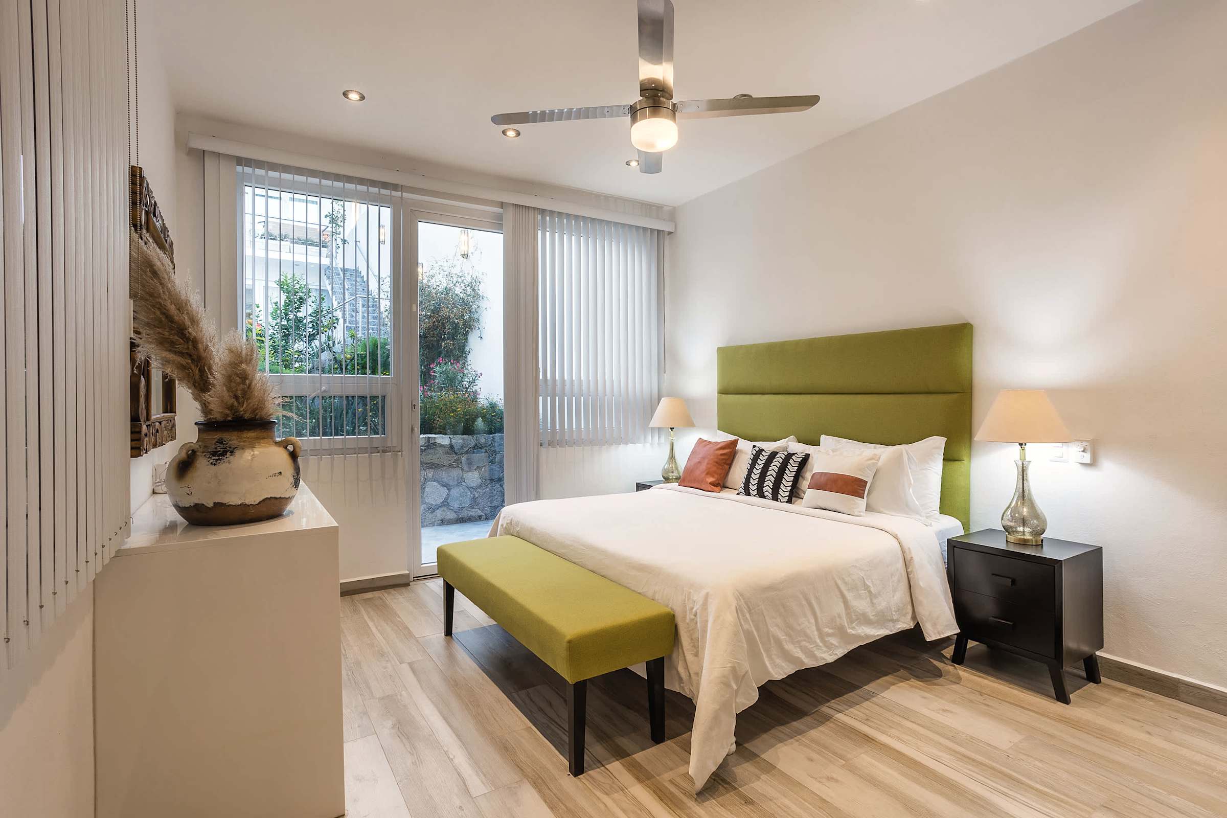 Recámara principal con cabecera verde, cama king y puertas de cristal hacia el jardín