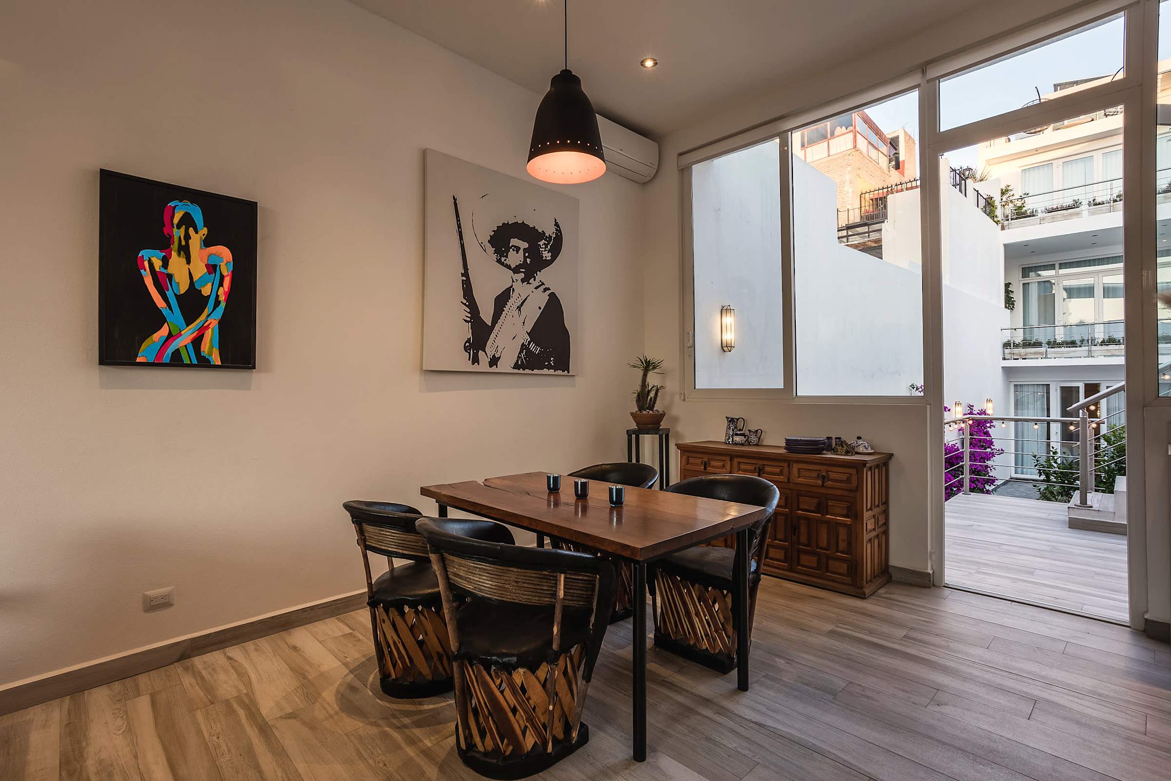 Comedor con mesa de madera, sillas equipales tejidas y acceso a terraza con vista a la ciudad