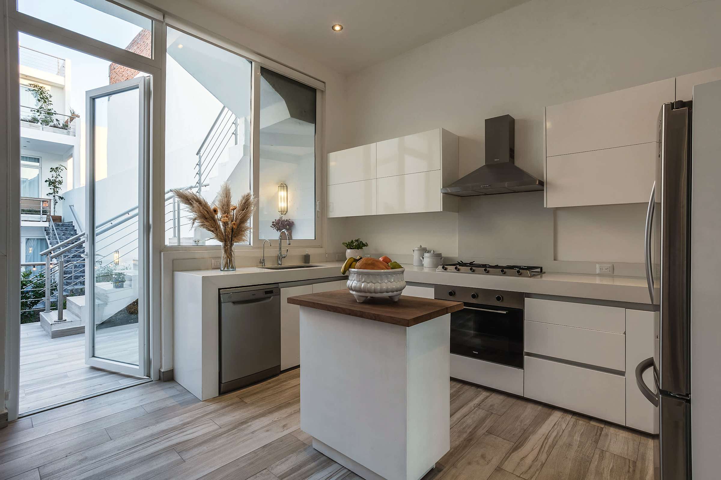 Cocina moderna con gabinetes blancos, isla central y puertas de vidrio hacia la terraza