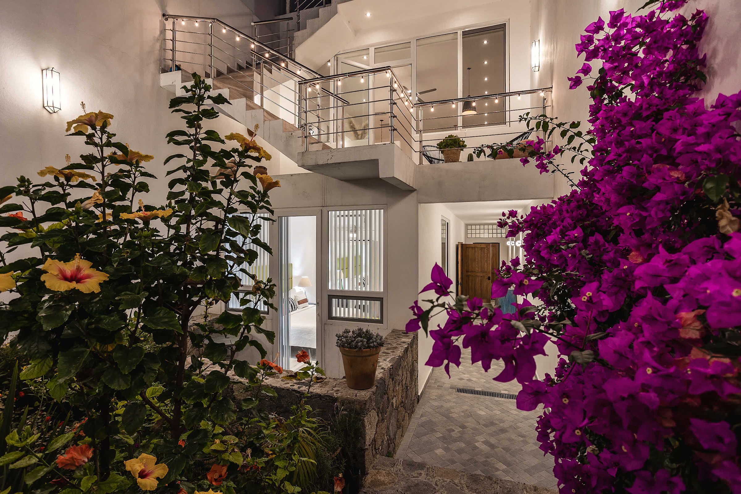 Patio con bugambilia magenta vibrante, flores amarillas y escalera de metal hacia nivel superior