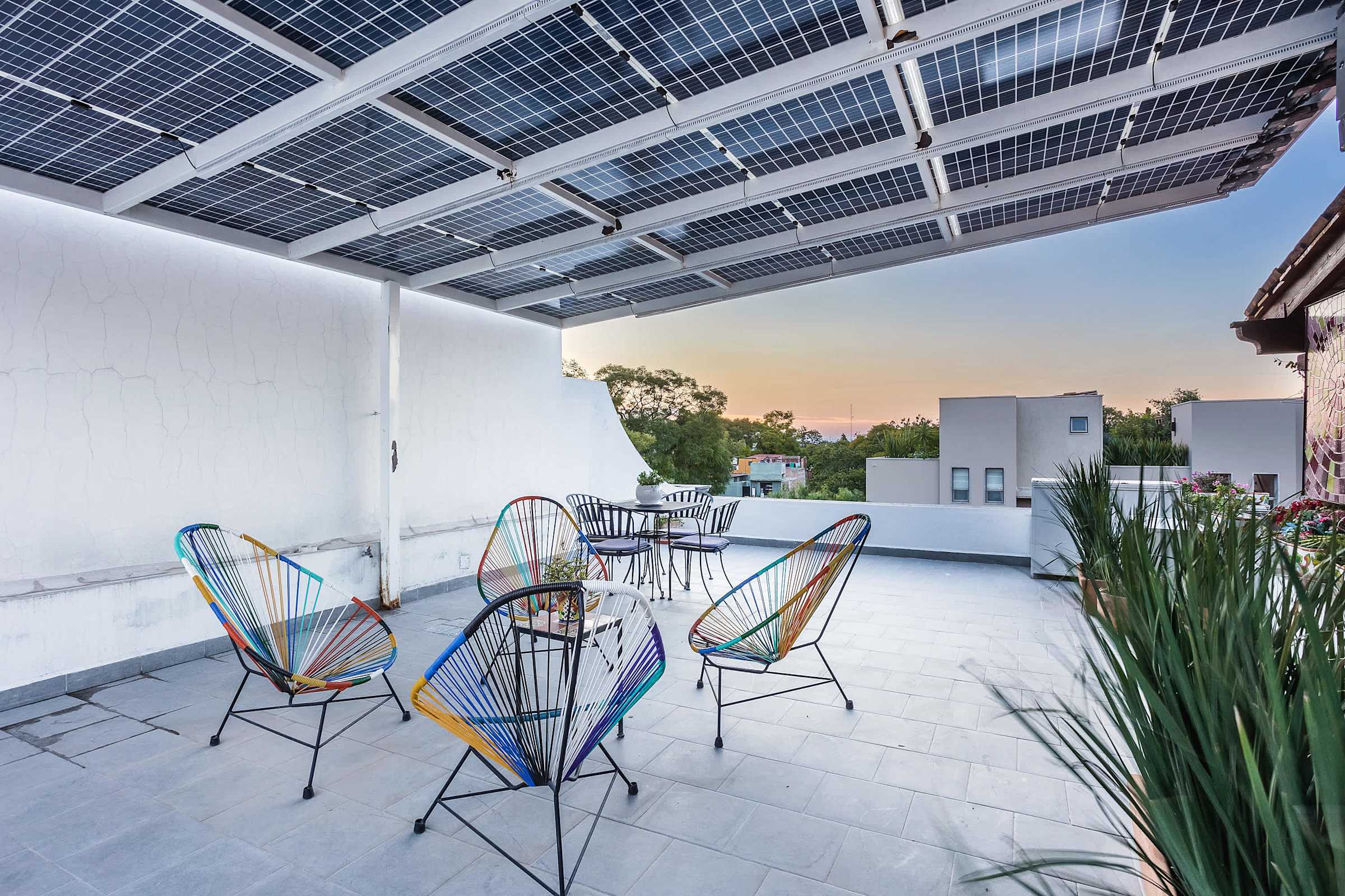 Terraza en la azotea con sillas de colores tejidas, paneles solares y vistas al atardecer sobre las colinas