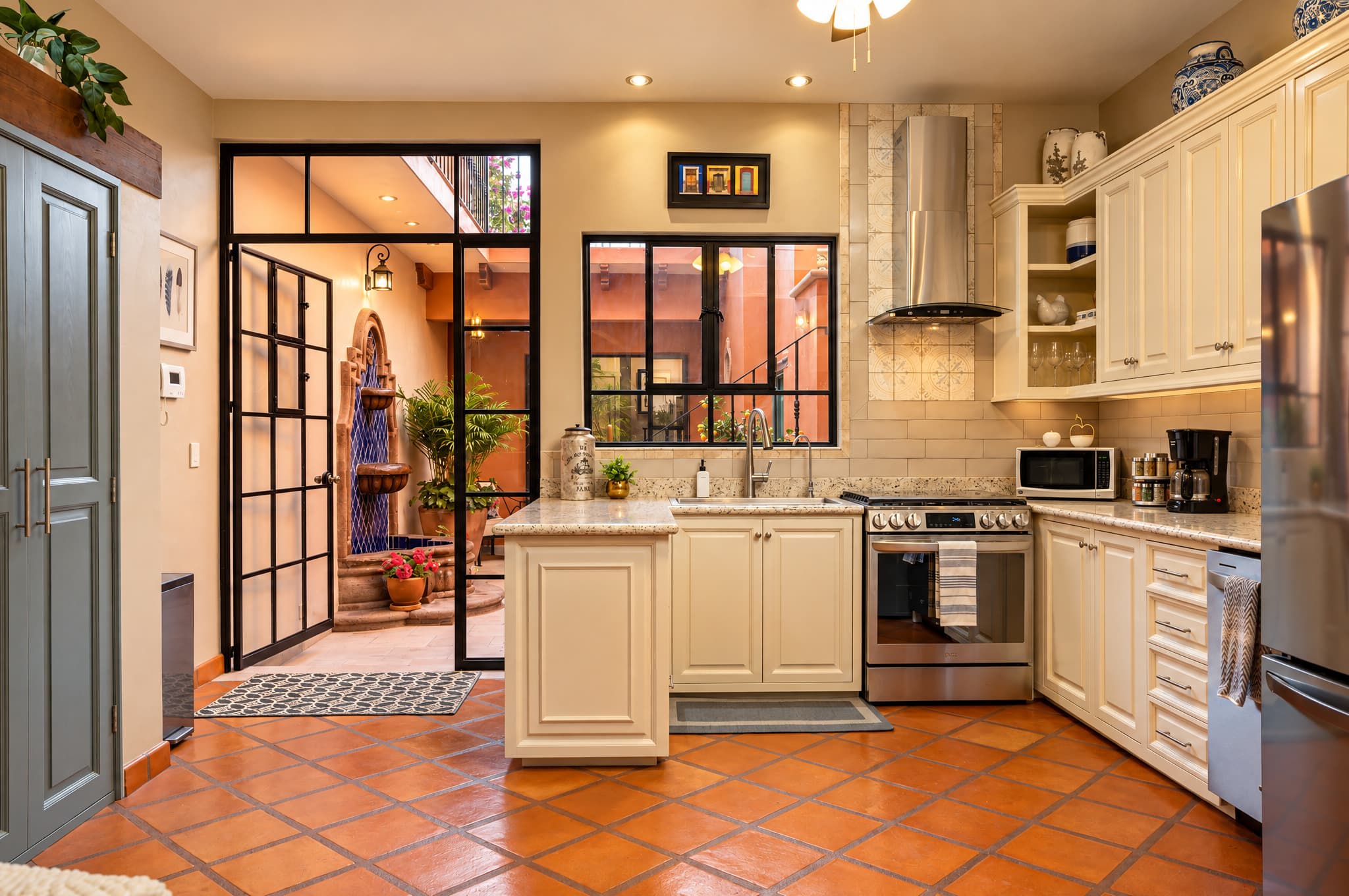Kitchen with cream cabinetry, terracotta tile floor, and black-framed door to courtyard