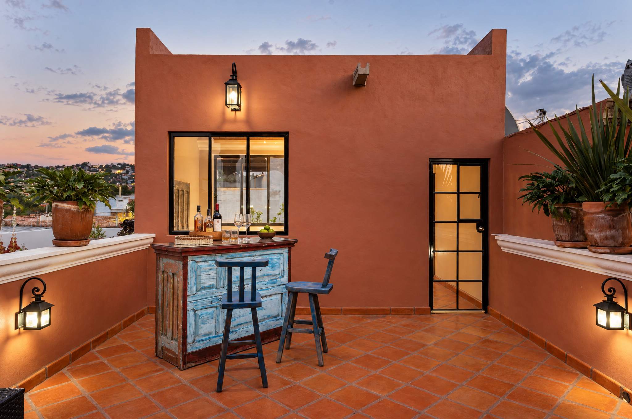 Rooftop bar with terracotta tiles, blue painted cabinet, and evening city views