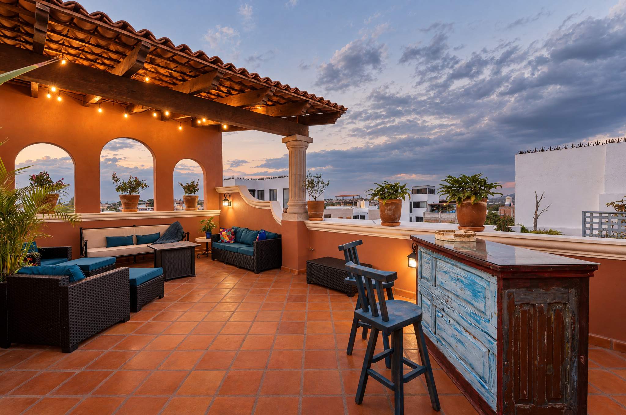 Rooftop lounge with arched windows, seating areas, and views over San Miguel de Allende at dusk