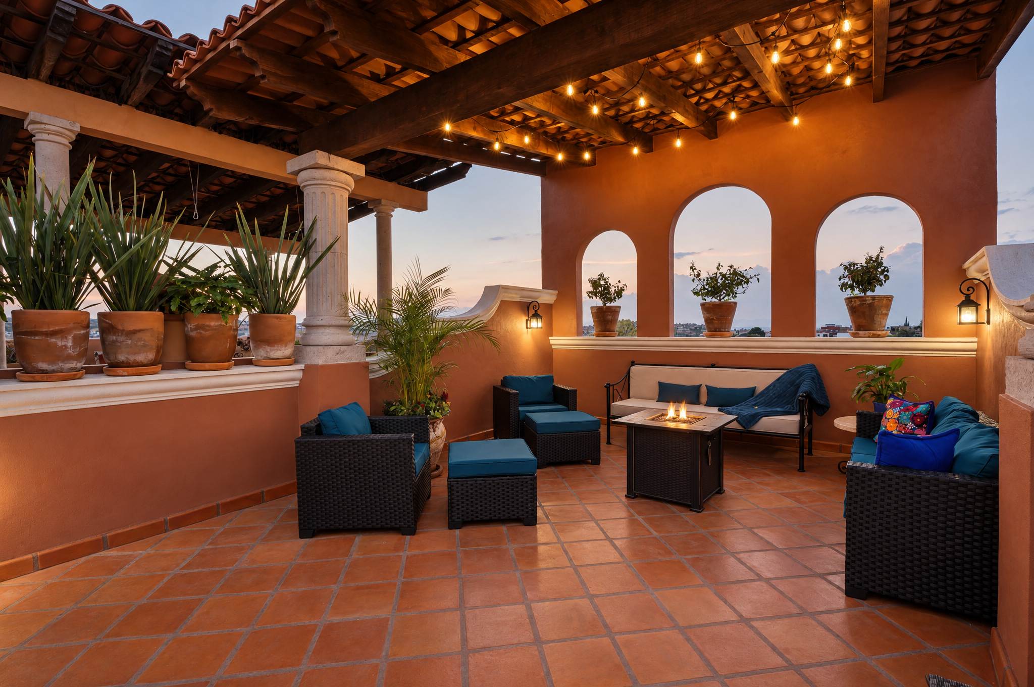 Rooftop terrace at dusk with blue seating, fireplace, and arched alcoves with potted plants