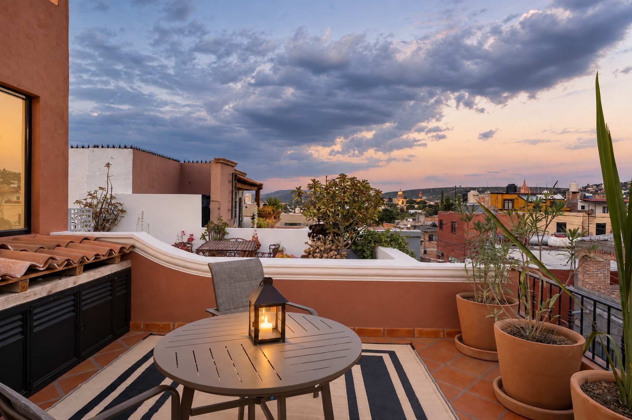 Rooftop terrace at dusk with round dining table, lantern lighting, and views of San Miguel de Allende