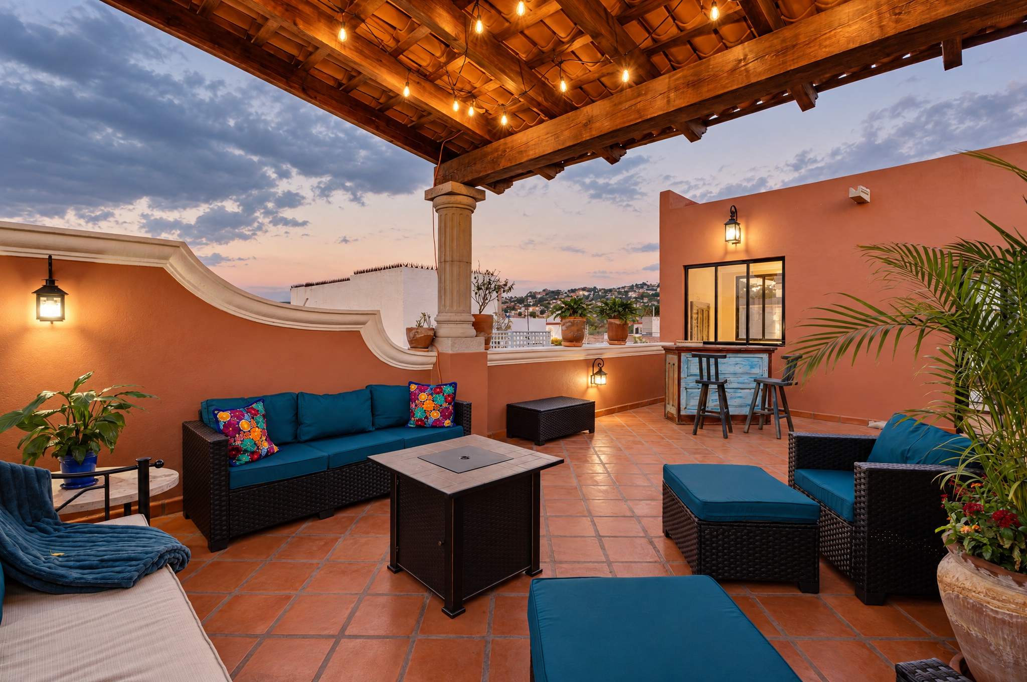 Rooftop terrace with blue sofas, fire pit table, and wooden pergola with ambient lighting