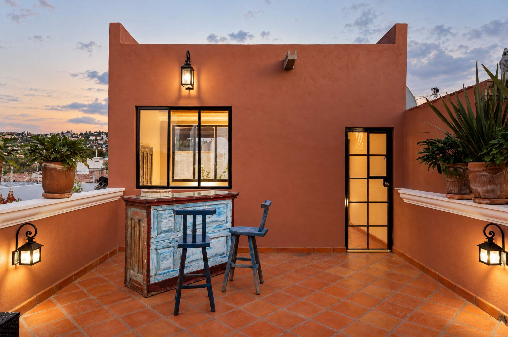 Rooftop terrace with orange walls, built-in bar with blue stools, and town views at dusk