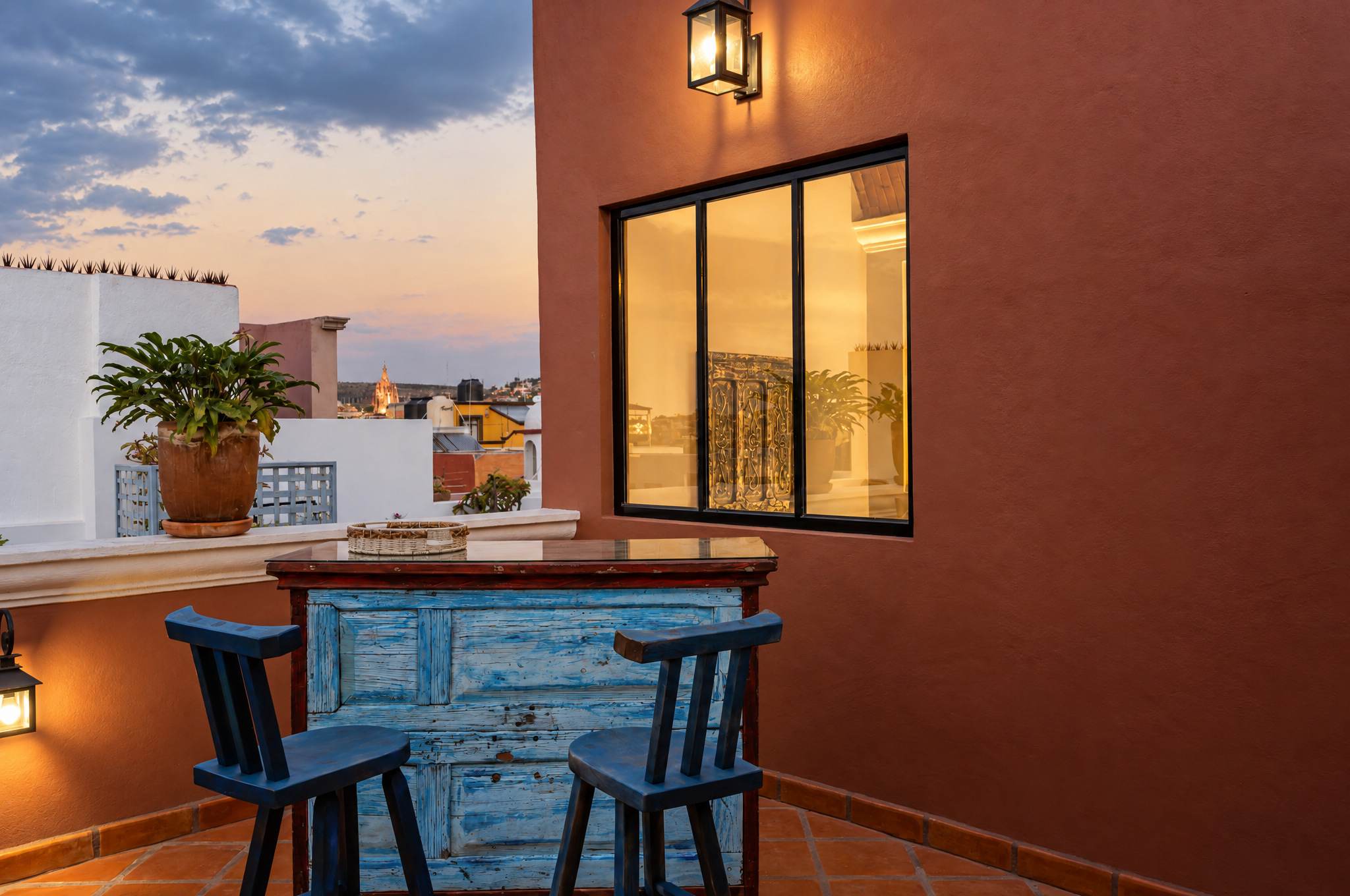 Rooftop bar with blue wooden counter, blue chairs, and view of the Parroquia at sunset