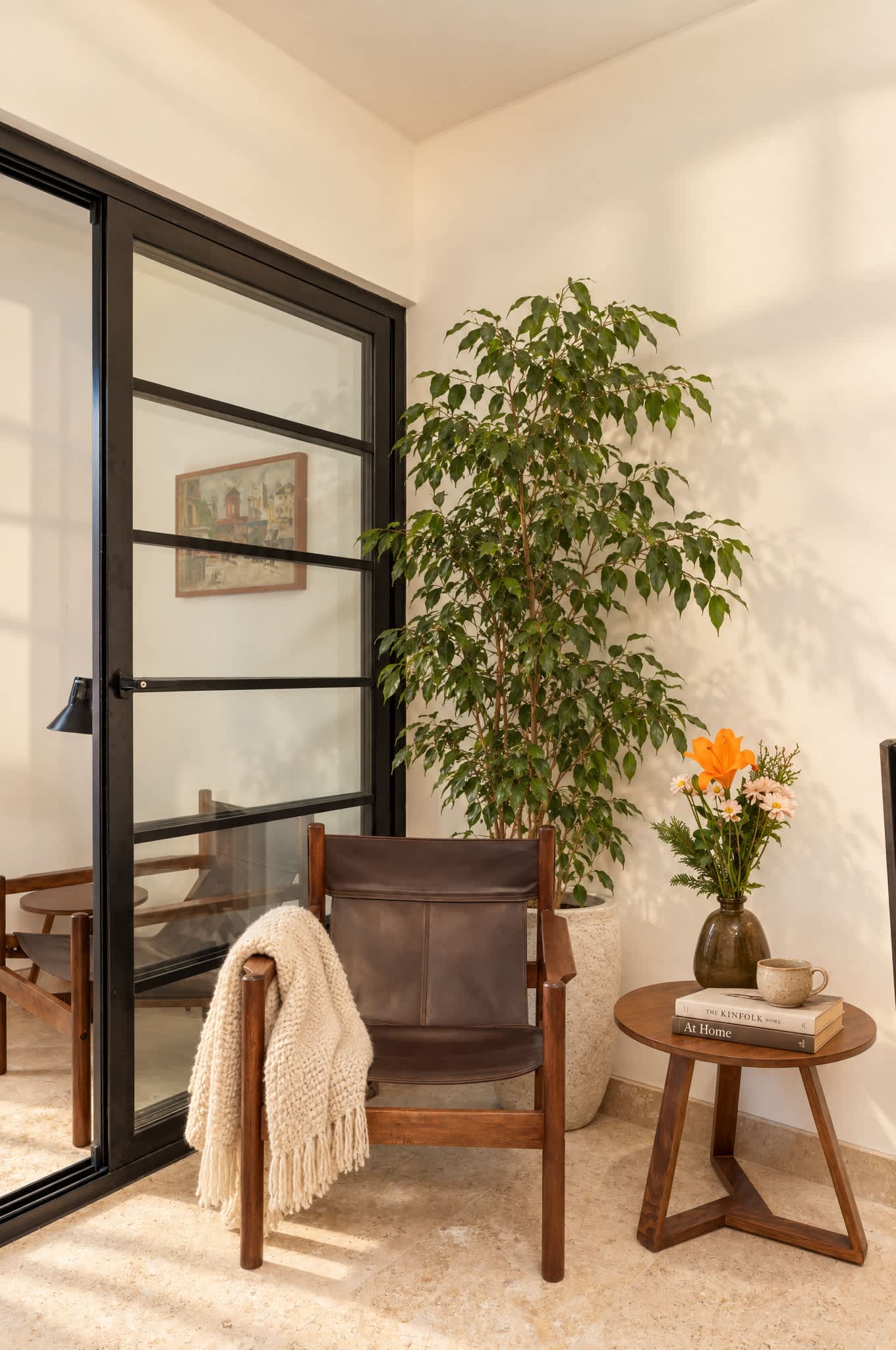 Rincón de lectura con sillón de cuero, mesa auxiliar de madera, planta en maceta y puertas de vidrio