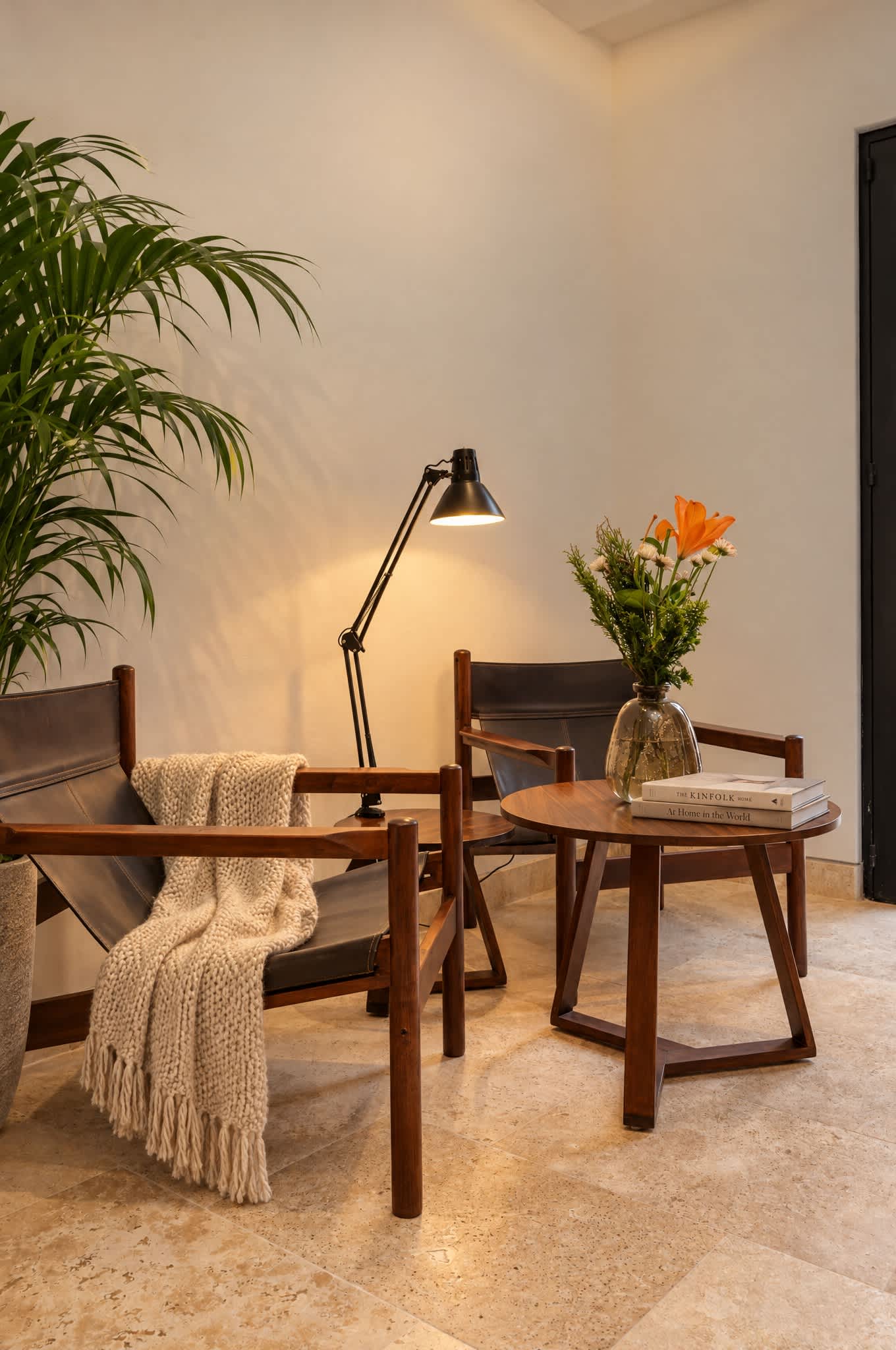 Rincón de lectura con sillas de madera, mesita auxiliar, lámpara de piso, flores frescas y planta en maceta