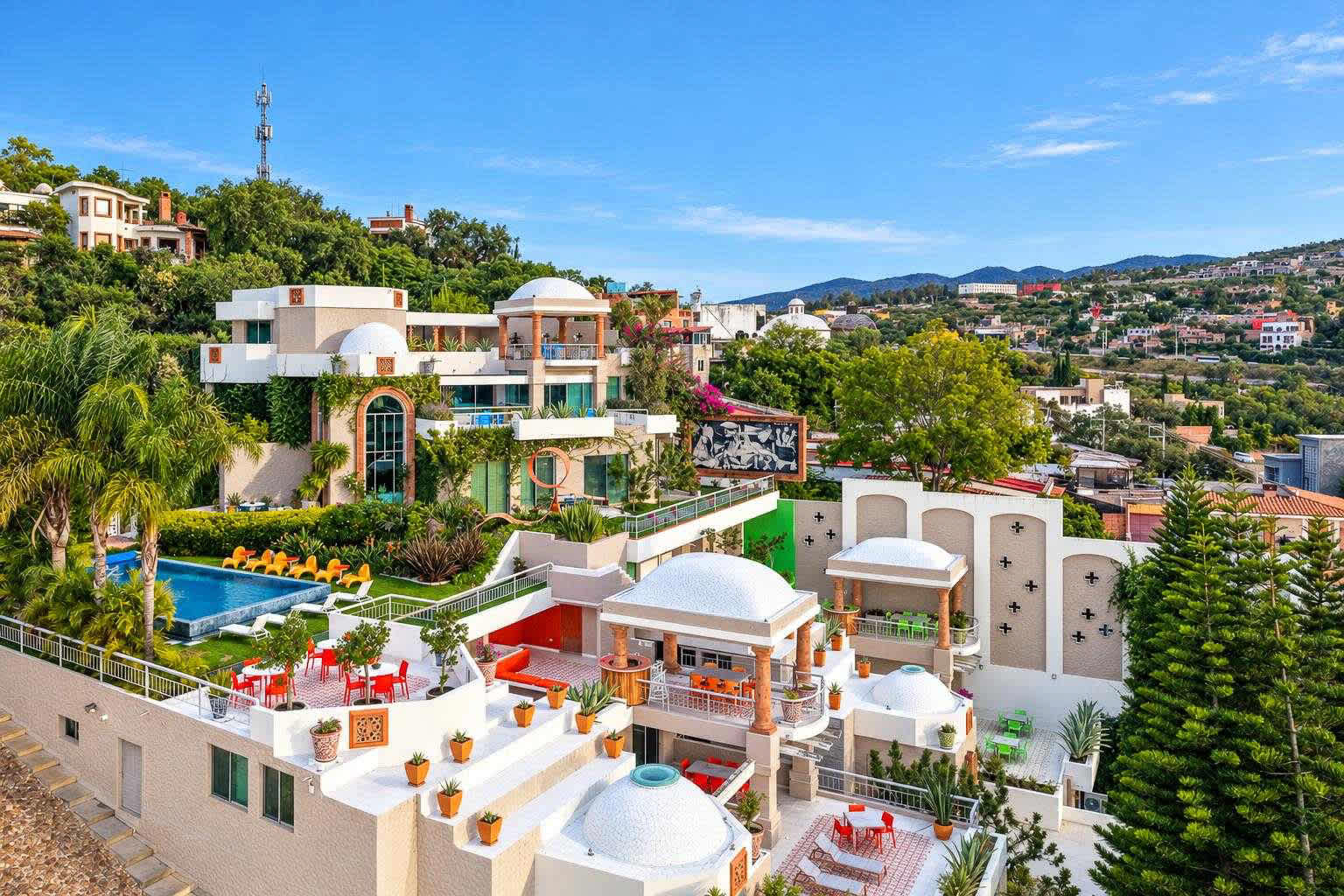 Aerial view of a multi-building estate with domed structures, terraces, swimming pool, and surrounding hillside landscape