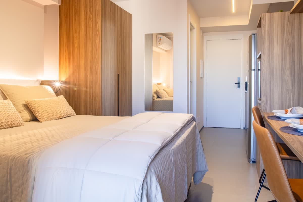 Studio moderno e funcional, com cama de casal, cozinha equipada e espaço para refeições ou home office.