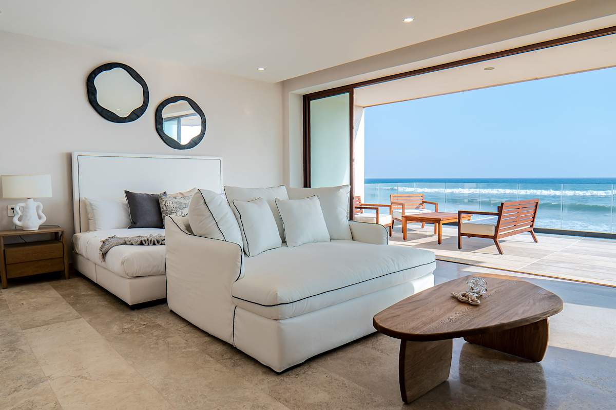 King suite sitting area with plush sofas, circular mirror wall art, and sweeping ocean views through glass walls