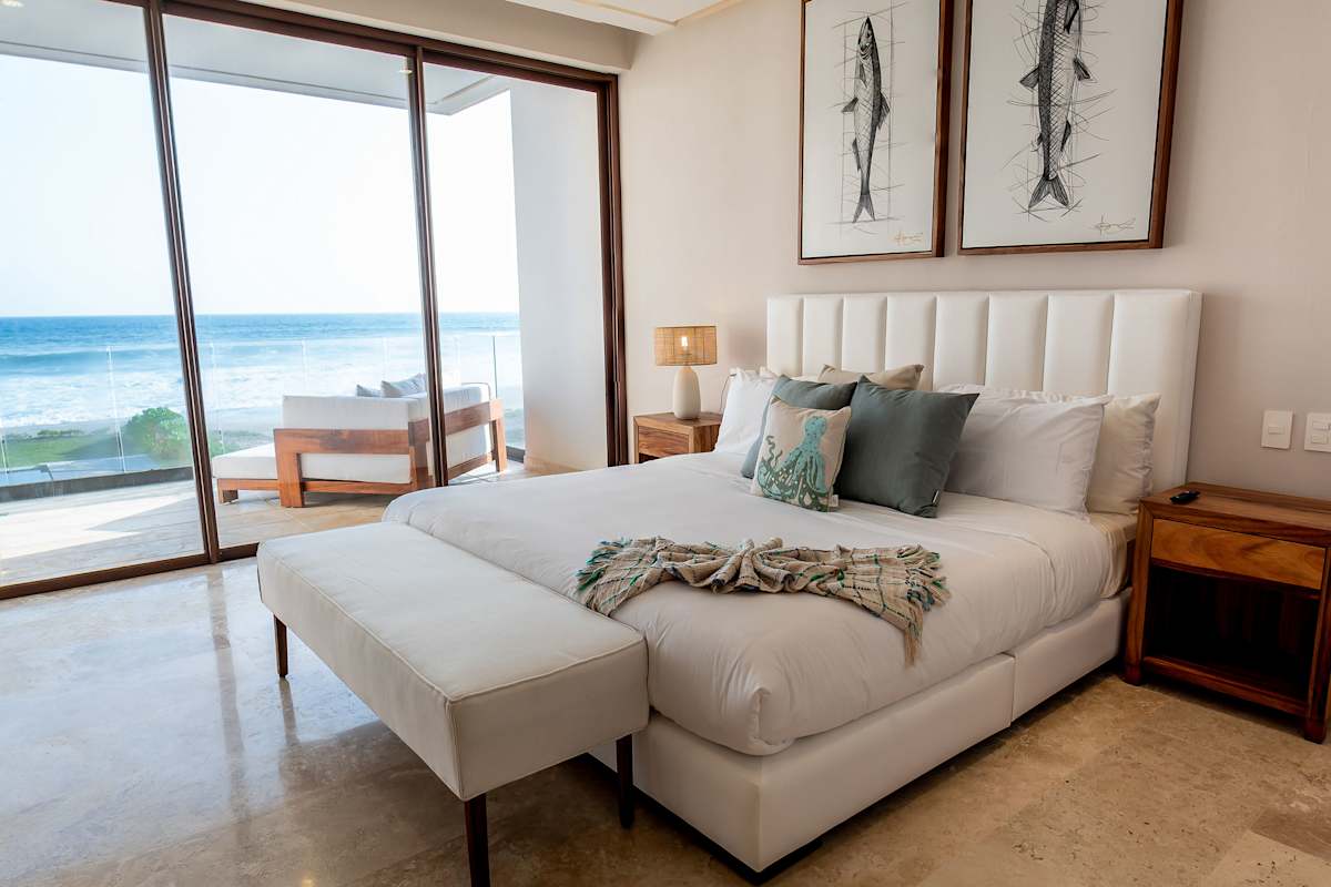 Bright king bedroom with coastal artwork, high-end linens, and direct ocean views through floor-to-ceiling windows