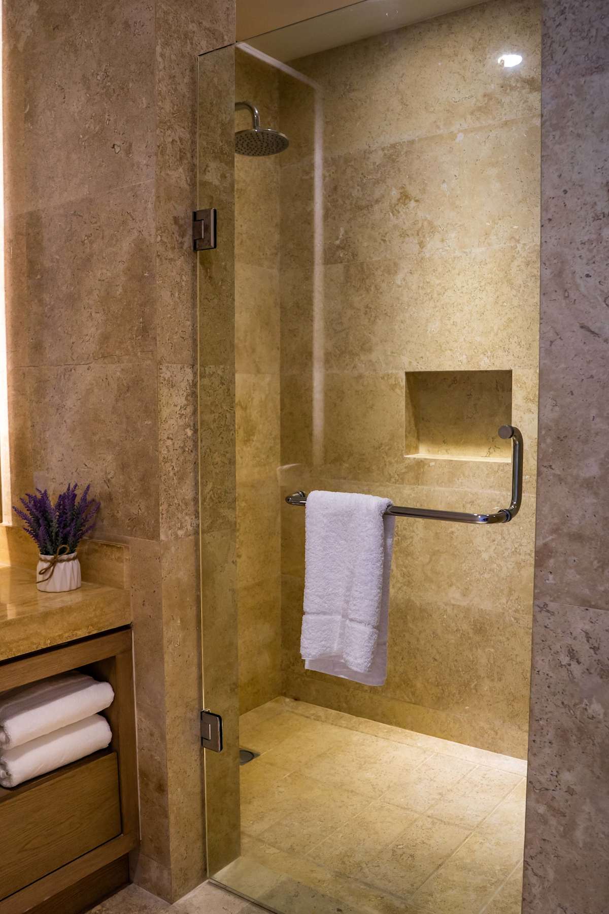 Walk-in stone-tiled shower with warm travertine finishes and hotel-quality towels provided