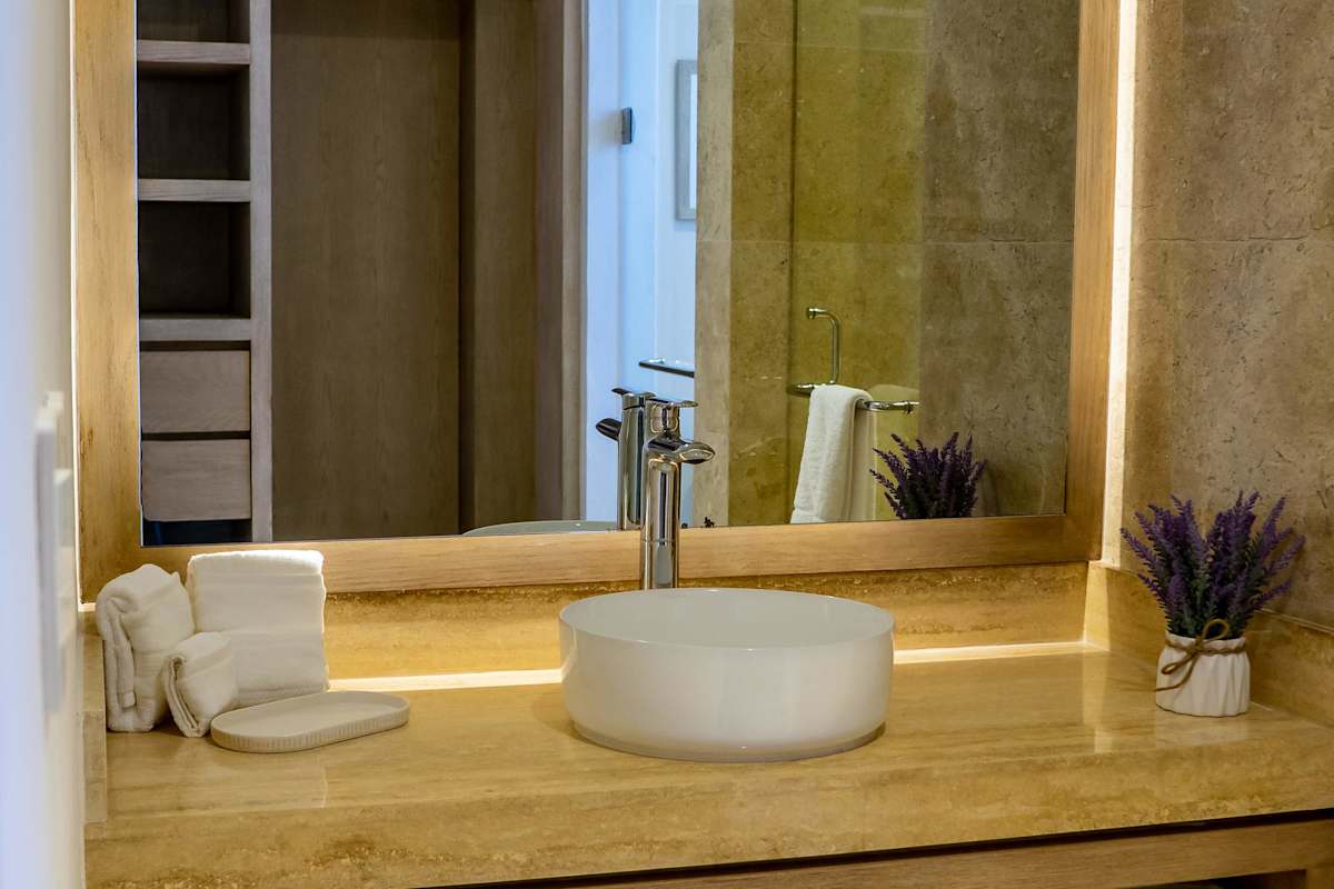 Luxurious marble-tiled bathroom with a wooden wardrobe and shower, warm gold tones, and lush plant accents