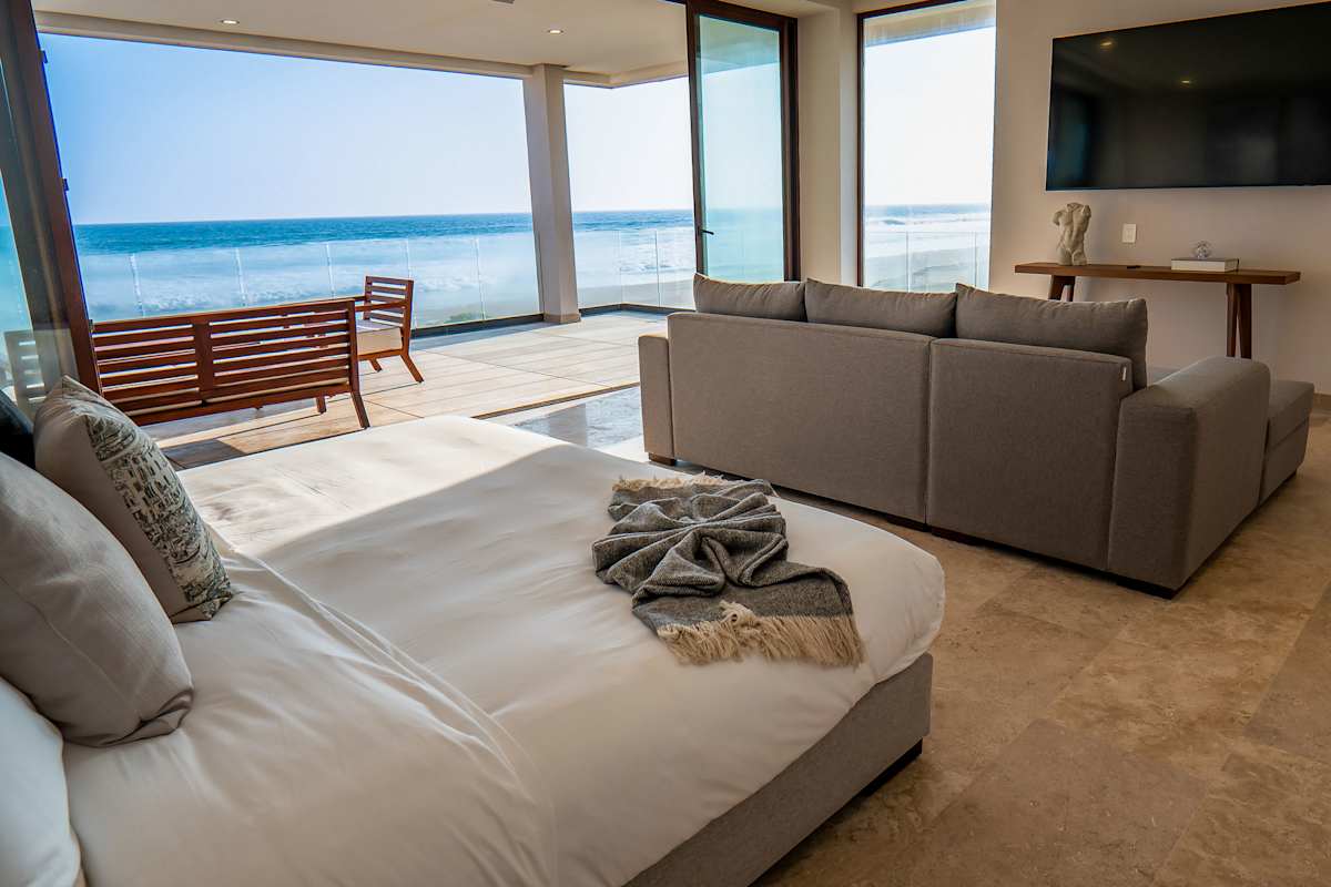 Bedroom 6 lounge area with a flat-screen TV, premium sofas, and beachfront views stretching to the horizon