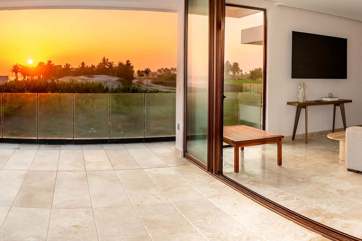 Bedroom with open glass doors capturing a fiery sunset, TV, and a balcony seat with orange horizon views