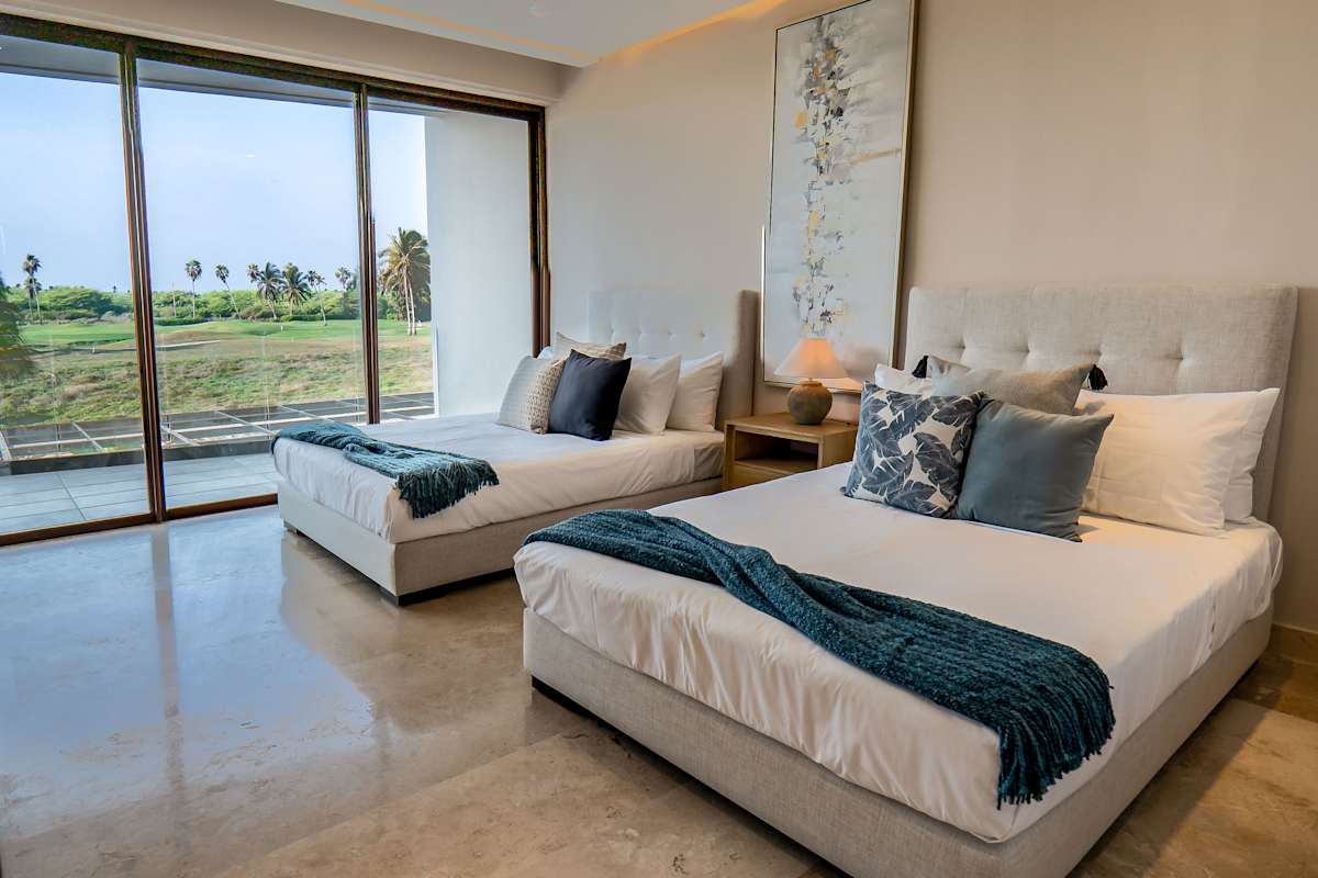 Bedroom 7 with two queen beds, tropical artwork, teal linens, and sliding glass doors to a private terrace that overlooks the golf course