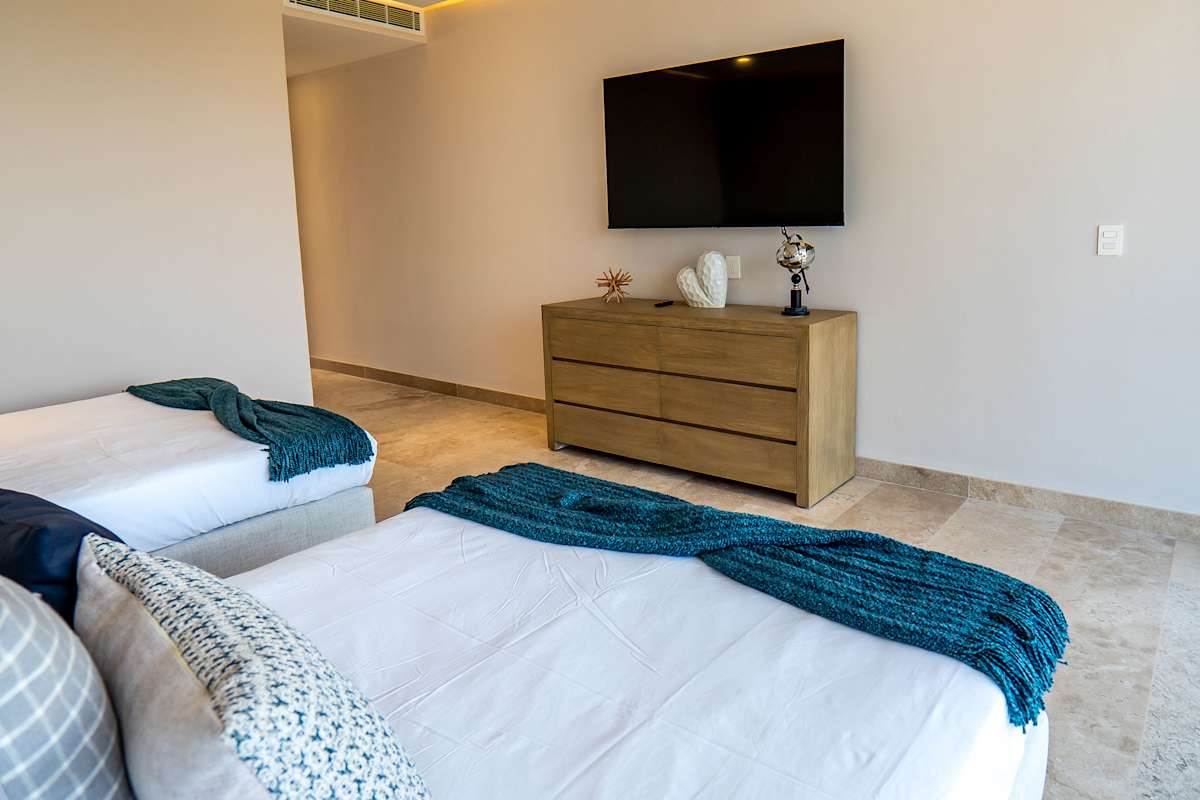 Bedroom 7 with two queen beds, teal accent bedding, TV, and wooden furniture — ideal for families or friends