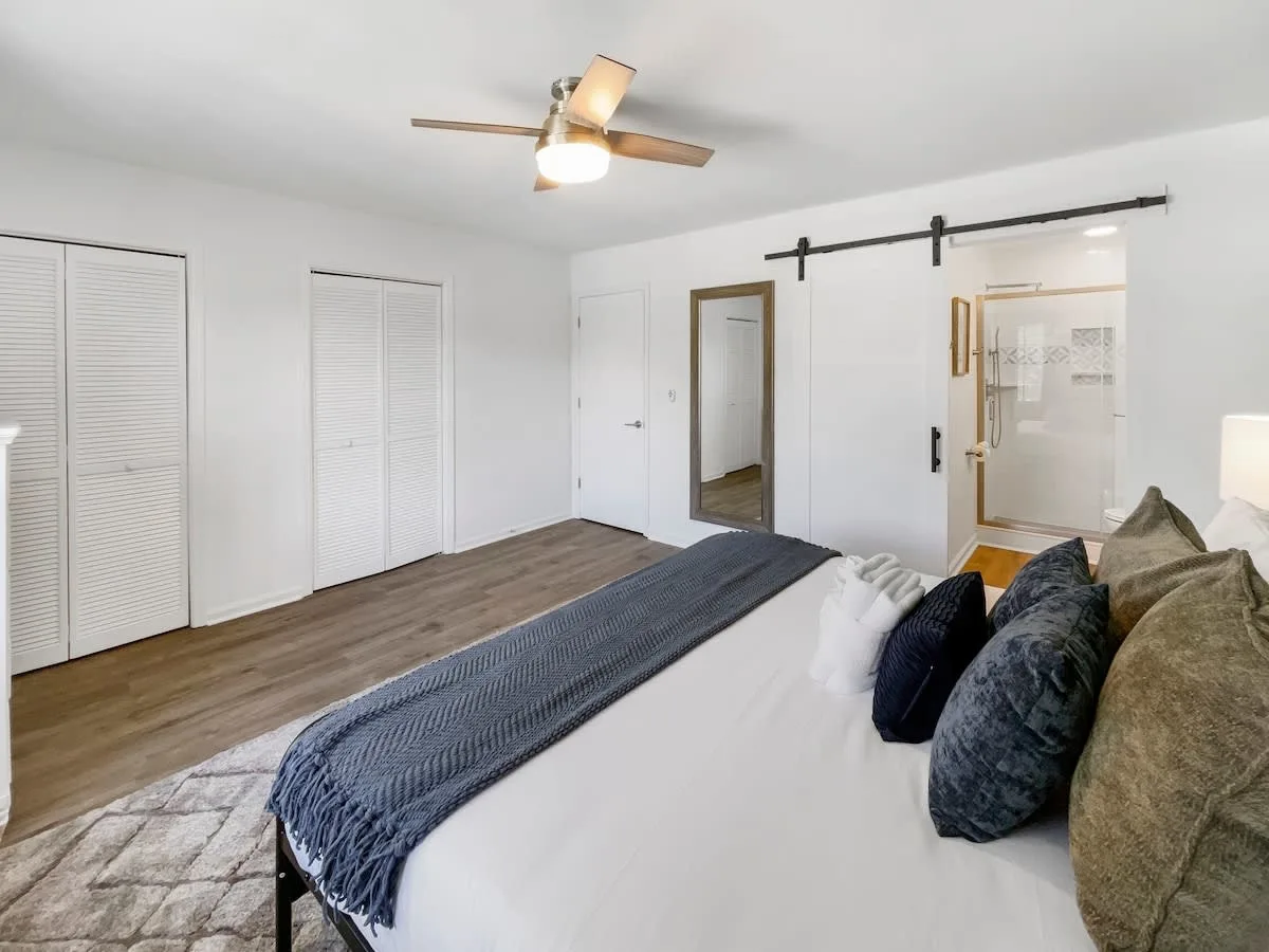A wide view of a bedroom with a bed, closet, and sliding barn door to the bathroom.