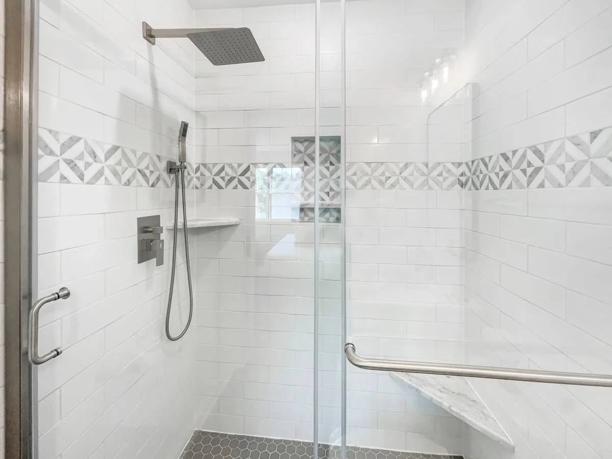 A clean and modern bathroom shower with white tile walls, a rainfall showerhead, and a glass door.
