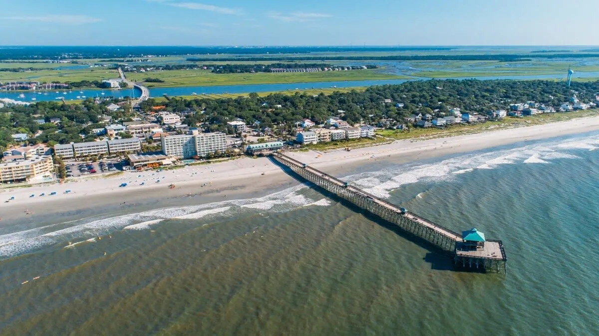Aerial view of a beach with a long pier and buildings in the background.