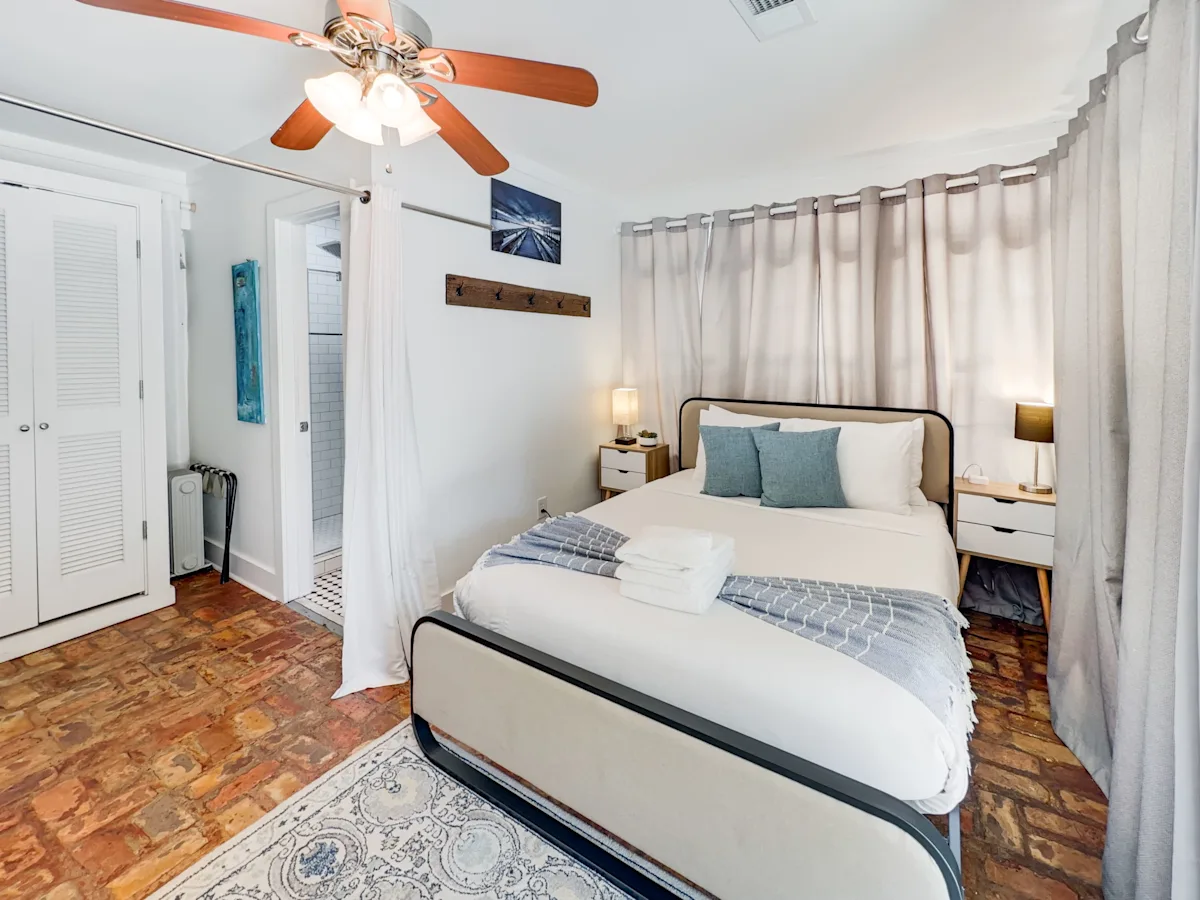 A wide view of a bedroom with a bed, nightstands, and a ceiling fan.