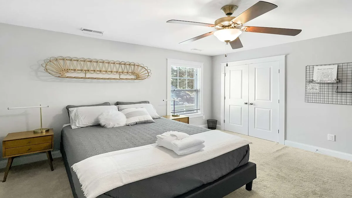 A neatly arranged bedroom with a gray bed, white pillows, and a ceiling fan.