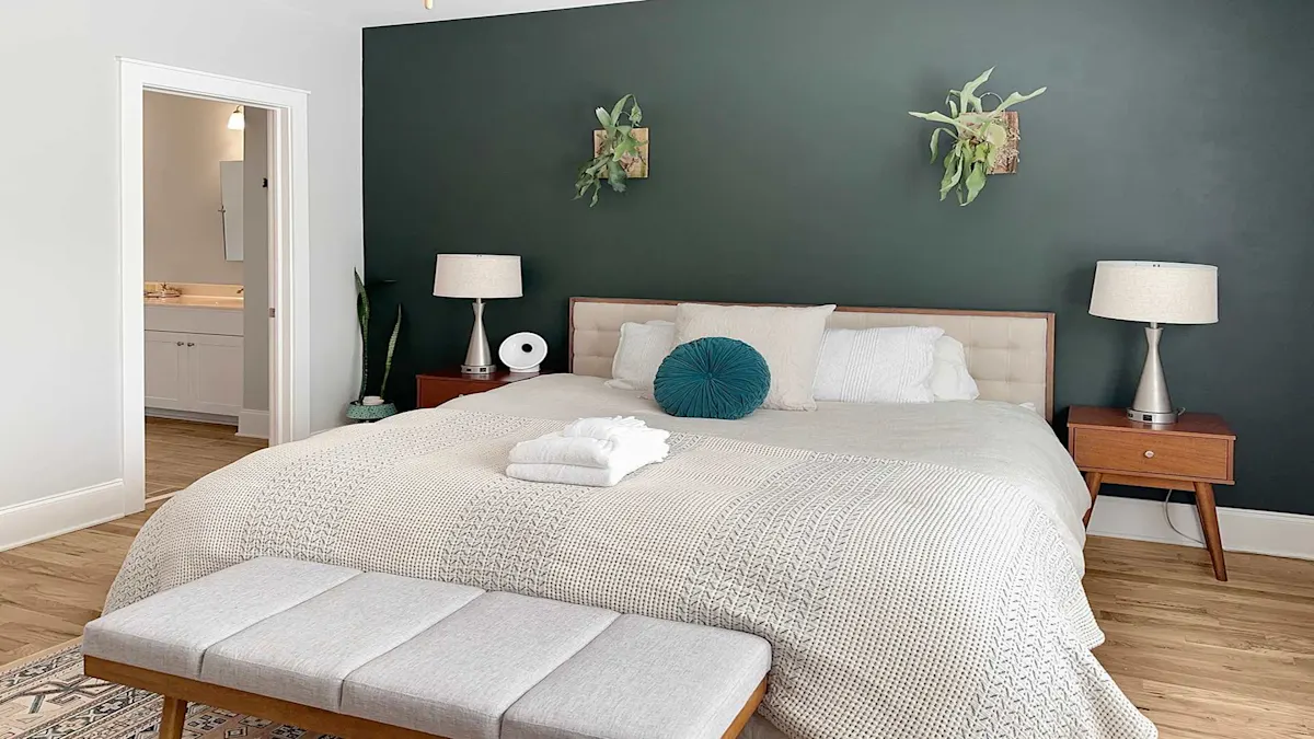 A wide view of a bedroom with a large bed, two nightstands, a bench at the foot of the bed, and a doorway to a bathroom.